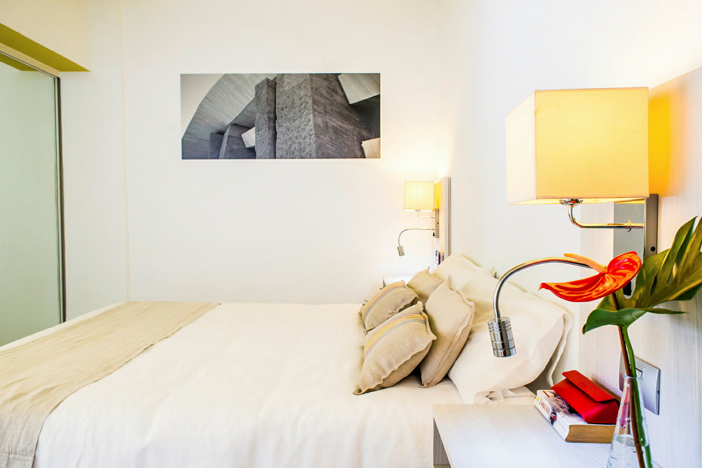 Et hotellrom med en dobbeltseng, lyse vegger, moderne interiør og en lese lampe på veggen. (AI-generert tekst)