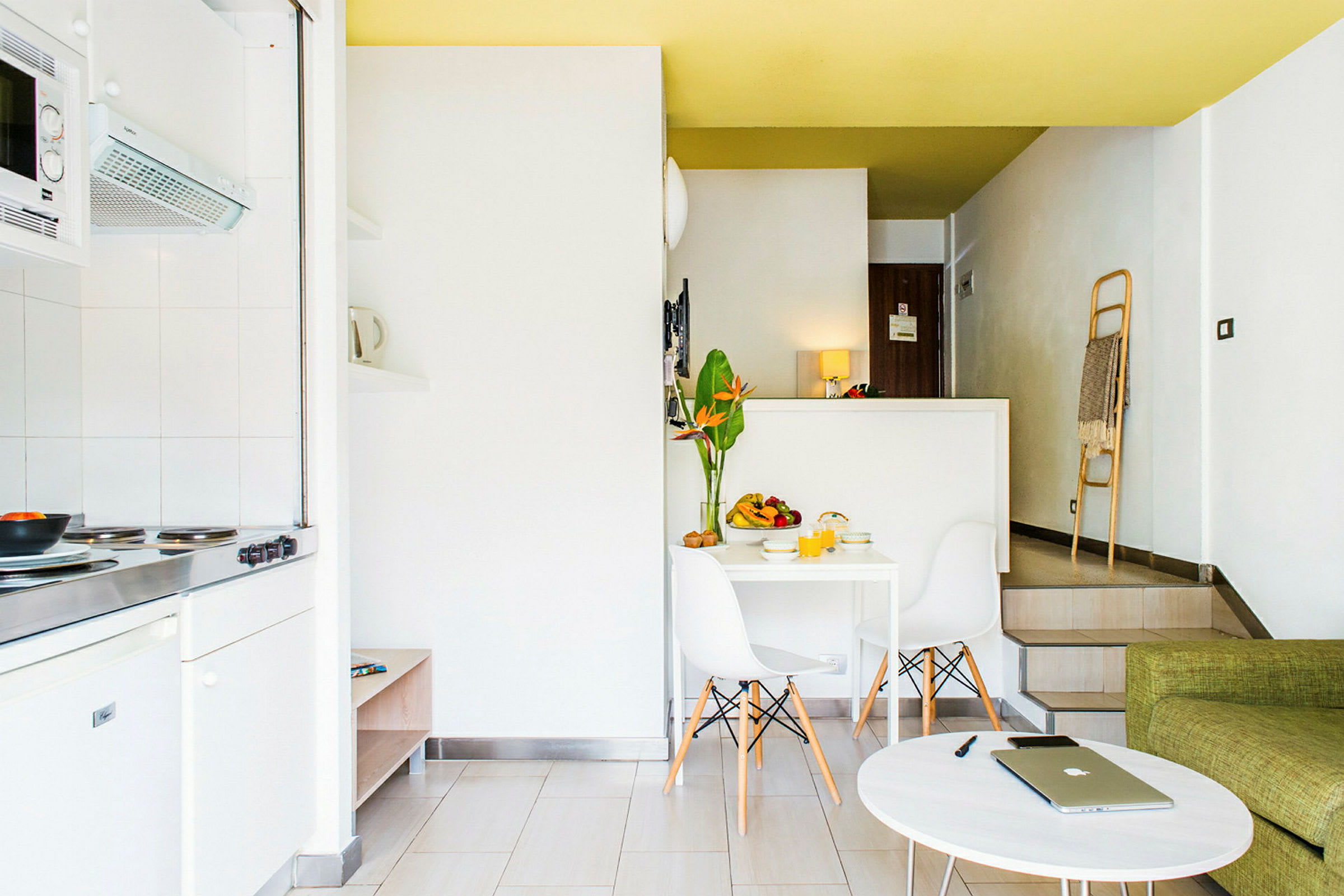 Et moderne og lyst innredet kjøkken og stue med hvite vegger, minimalistisk møblering og dekorative elementer, inkludert en vase med planter på et spisebord. (AI-generert tekst)