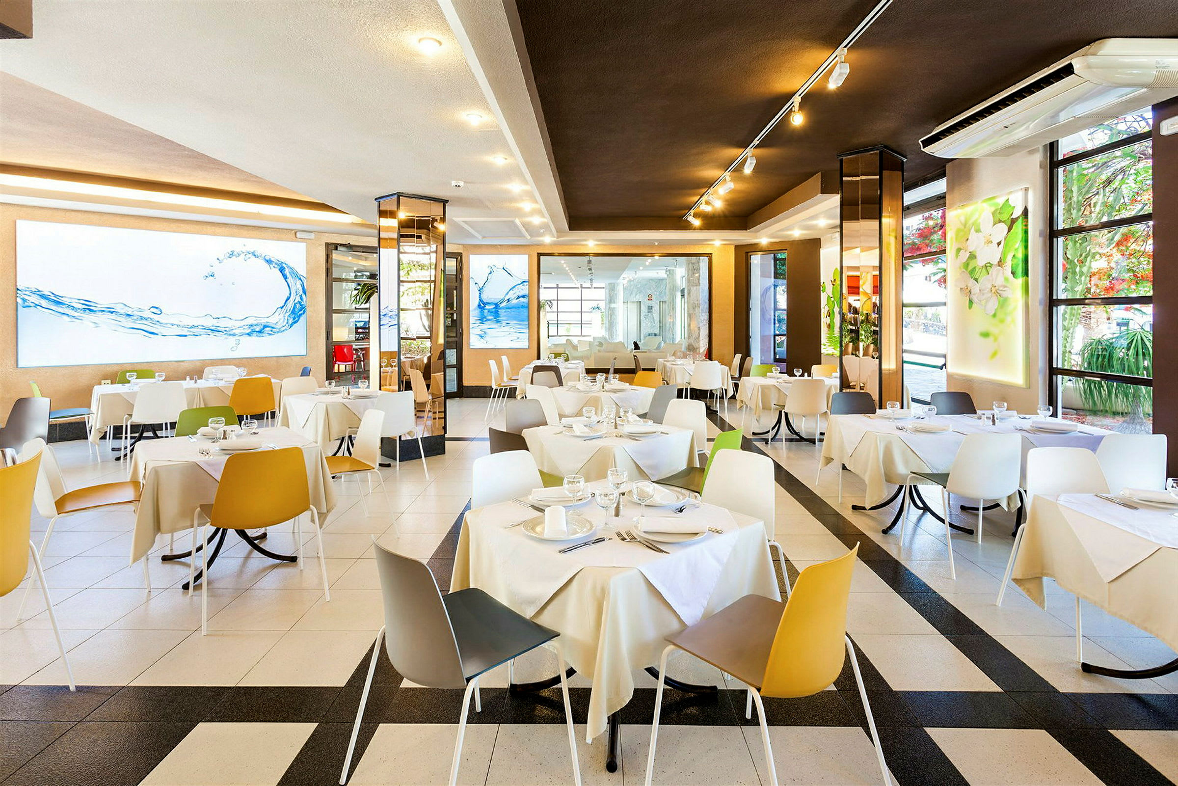 Et lyst og moderne restaurantområde med bord og stoler i ulike farger. (AI-generert tekst)