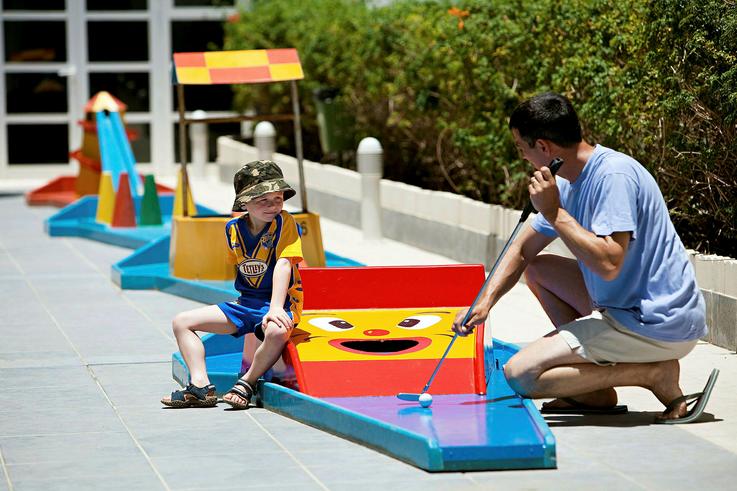 Personer spiller minigolf utendørs på en bane med fargerike hindringer. (AI-generert tekst)