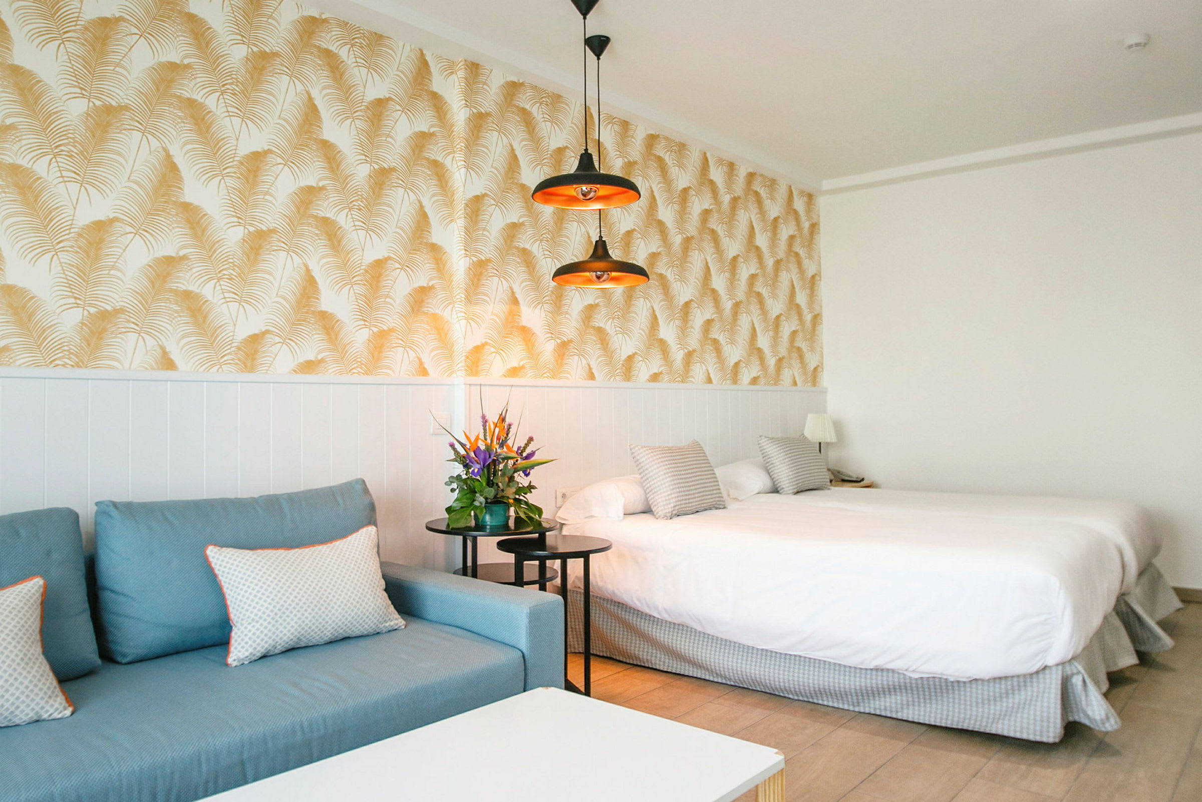 Hotellrom med blå sofa, dobbeltseng og dekorativt tapet. (AI-generert tekst)
