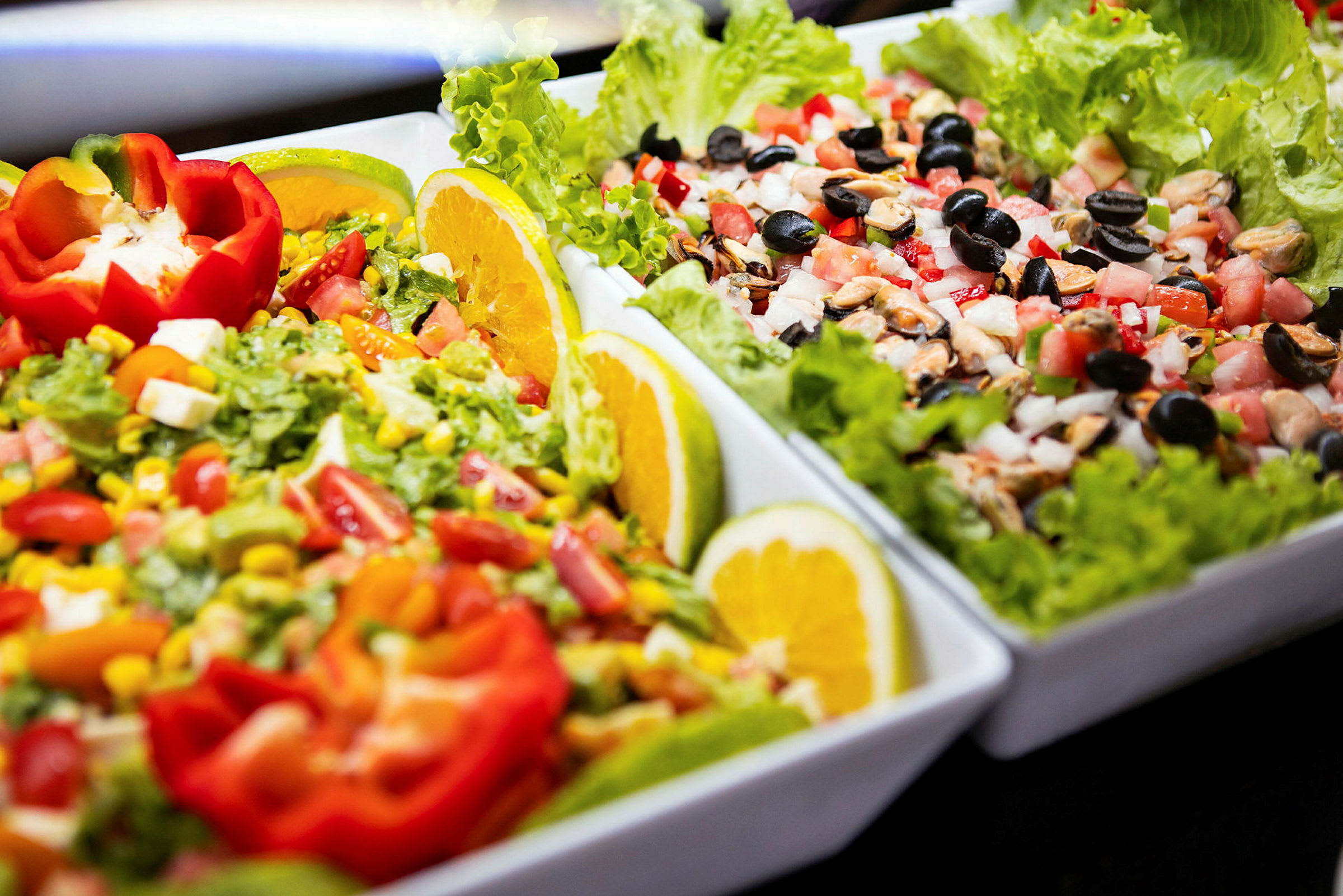 To fat fylt med fargerike salatingredienser, inkludert tomater, mais, oliven og salatblader, dekorert med sitronskiver og paprika. (AI-generert tekst)