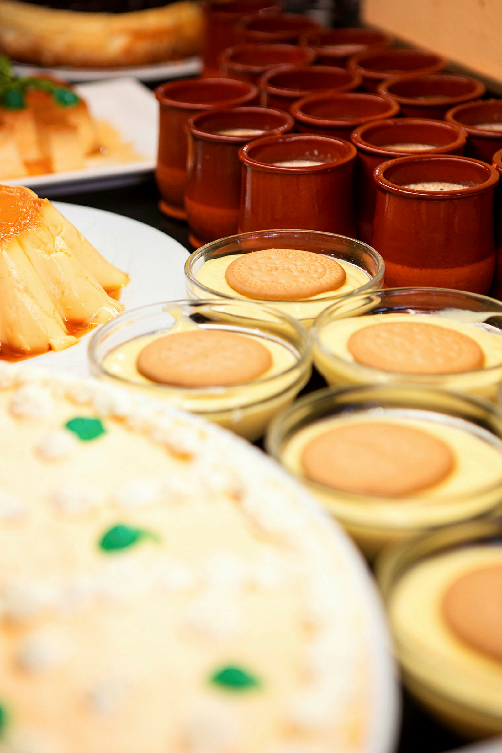 En rekke små skåler med dessert toppet med kjeks, bak vises flere desserter og små krukker. (AI-generert tekst)