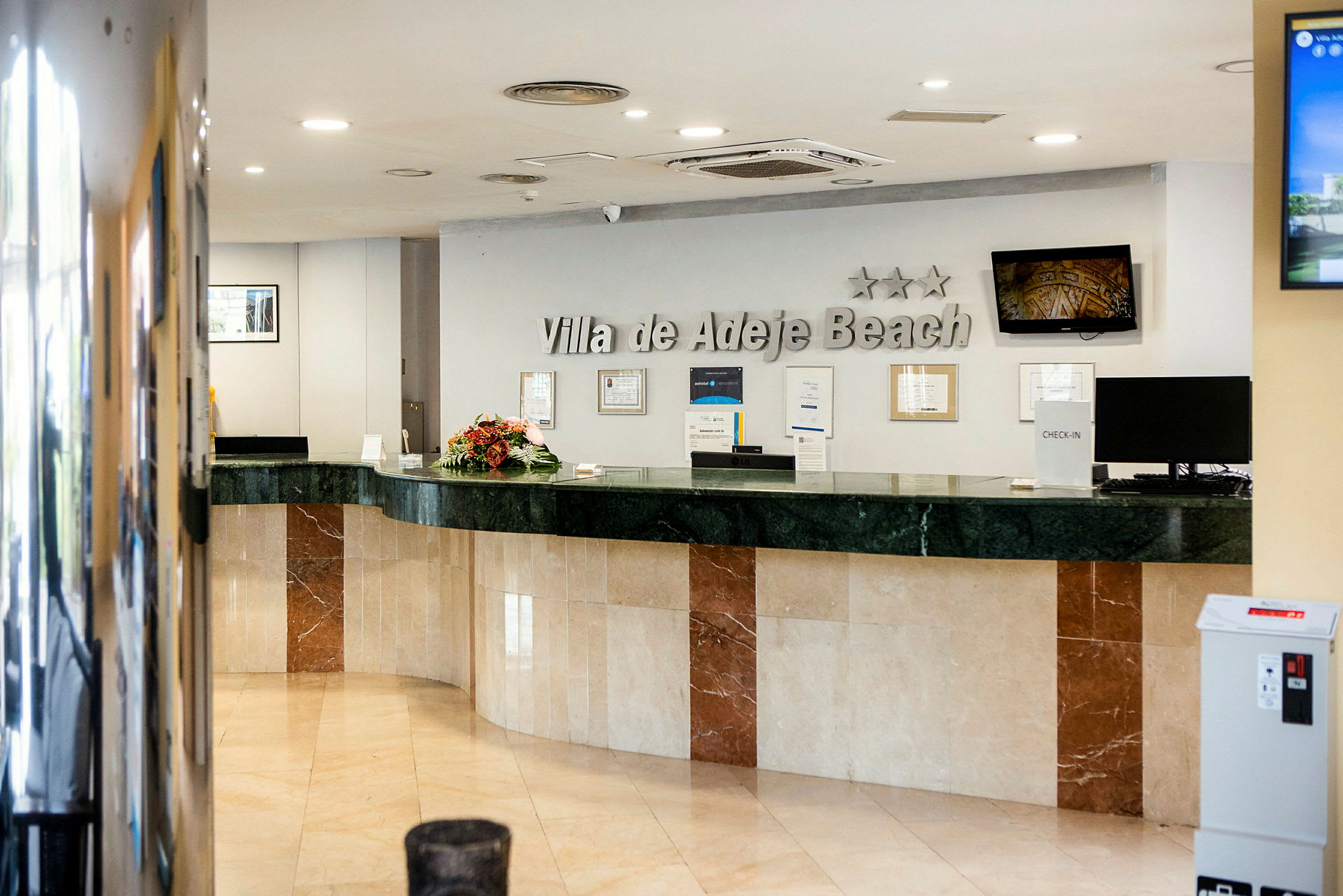 Hotellresepsjon med marmordisk og skilt som viser "Villa de Adeje Beach". (AI-generert tekst)