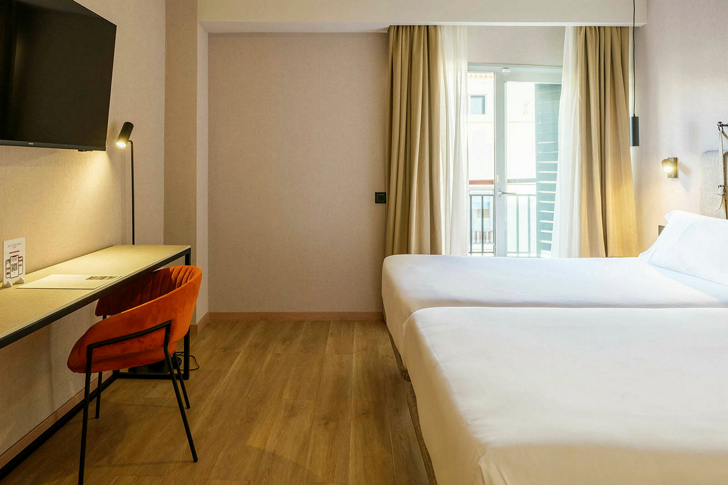 Et hotellrom med to senger, skrivebord og stol. (AI-generert tekst)