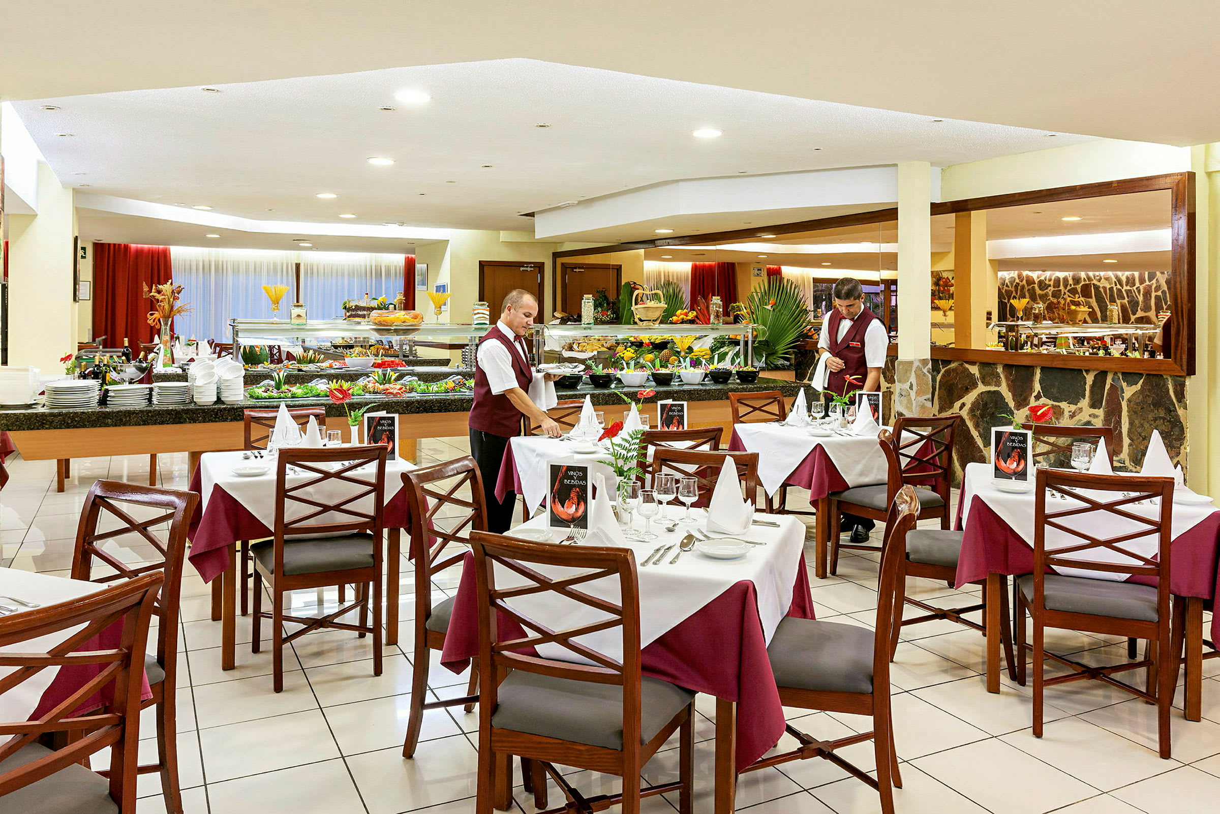 En restaurant med dekkede bord, velutstyrte bufféområder og en servitør i uniform. (AI-generert tekst)
