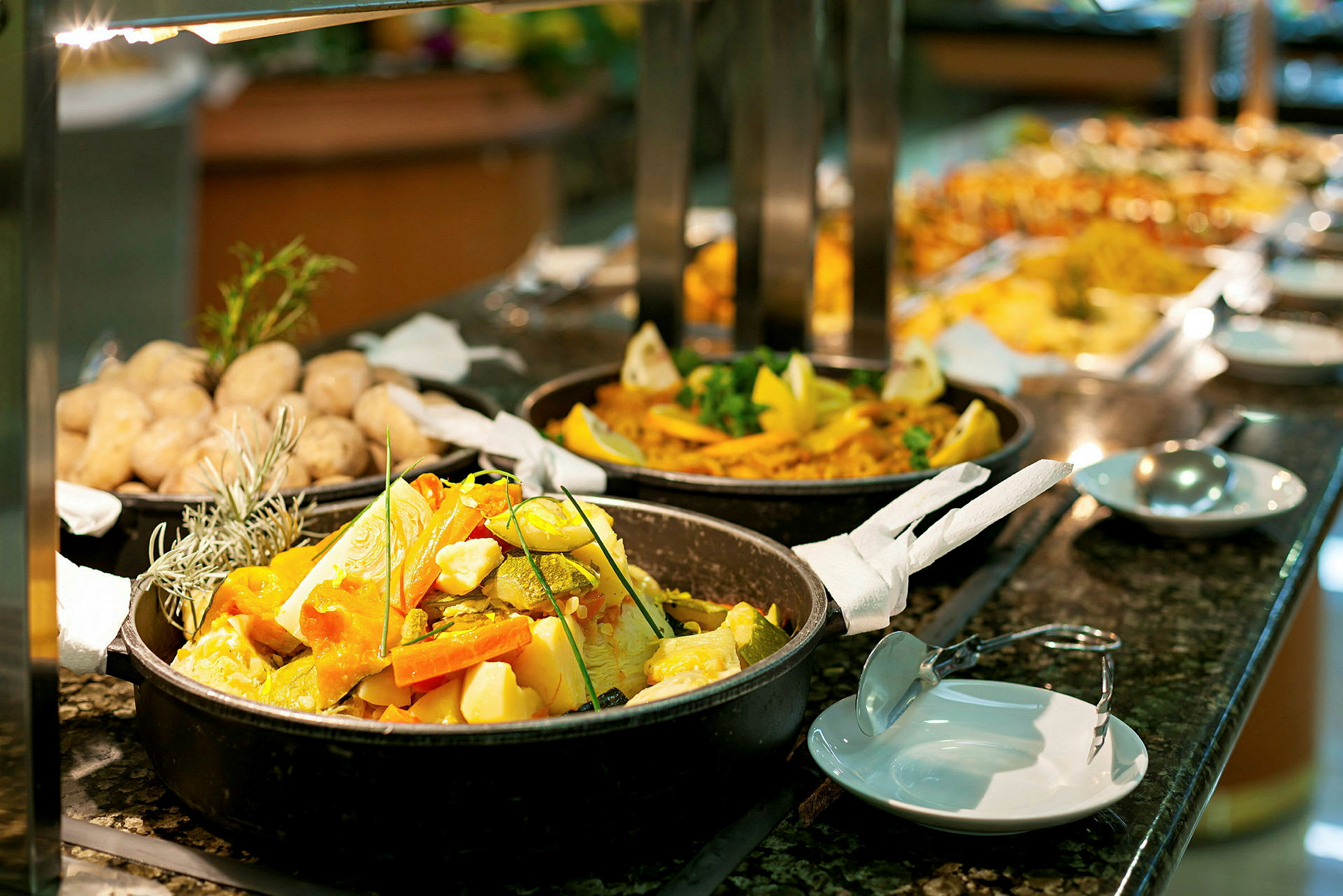 Buffet med ulike retter, inklusive grønnsaker i en gryte og bakte poteter. (AI-generert tekst)