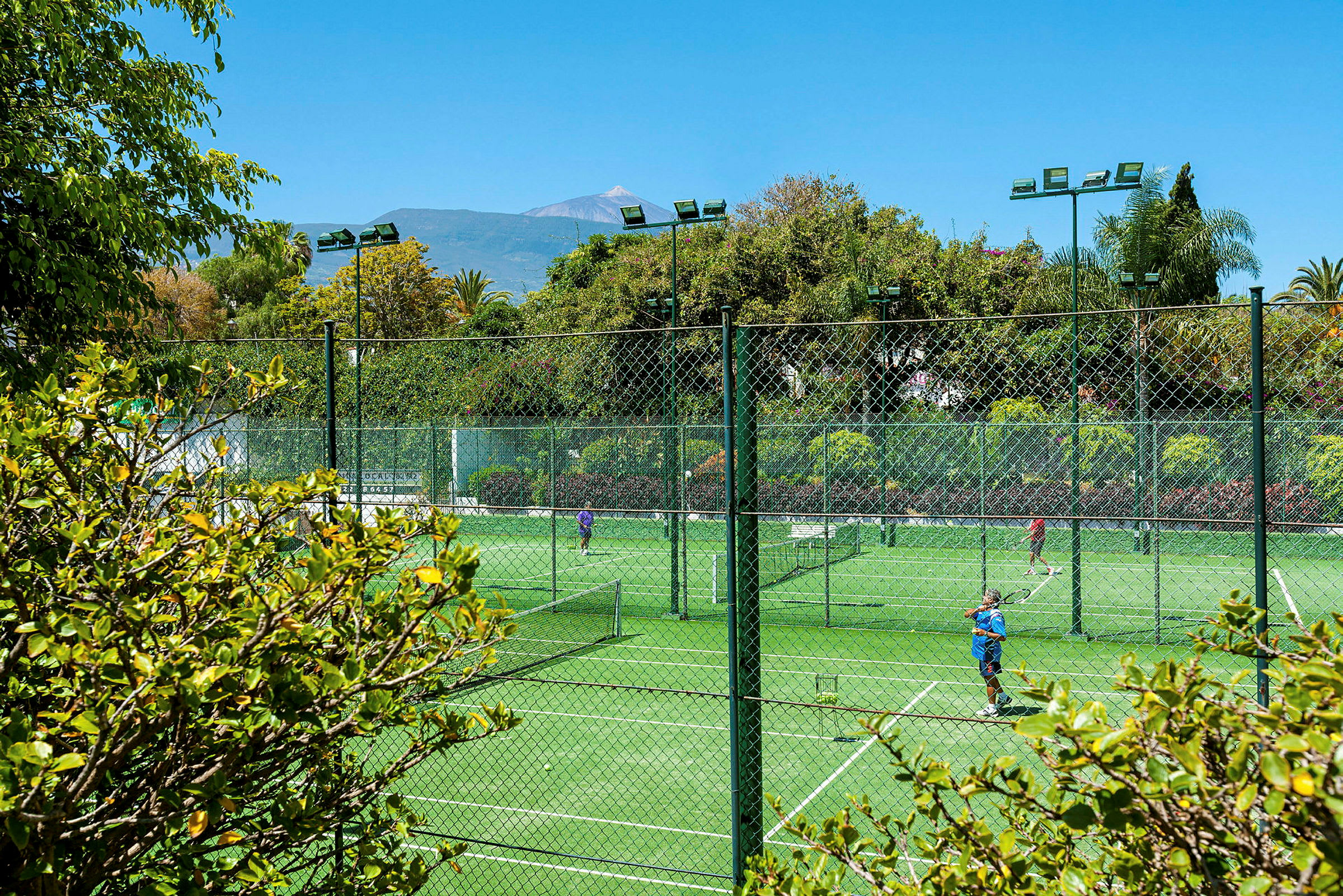 Utendørs tennisbaner omgitt av grøntområder og trær. (AI-generert tekst)