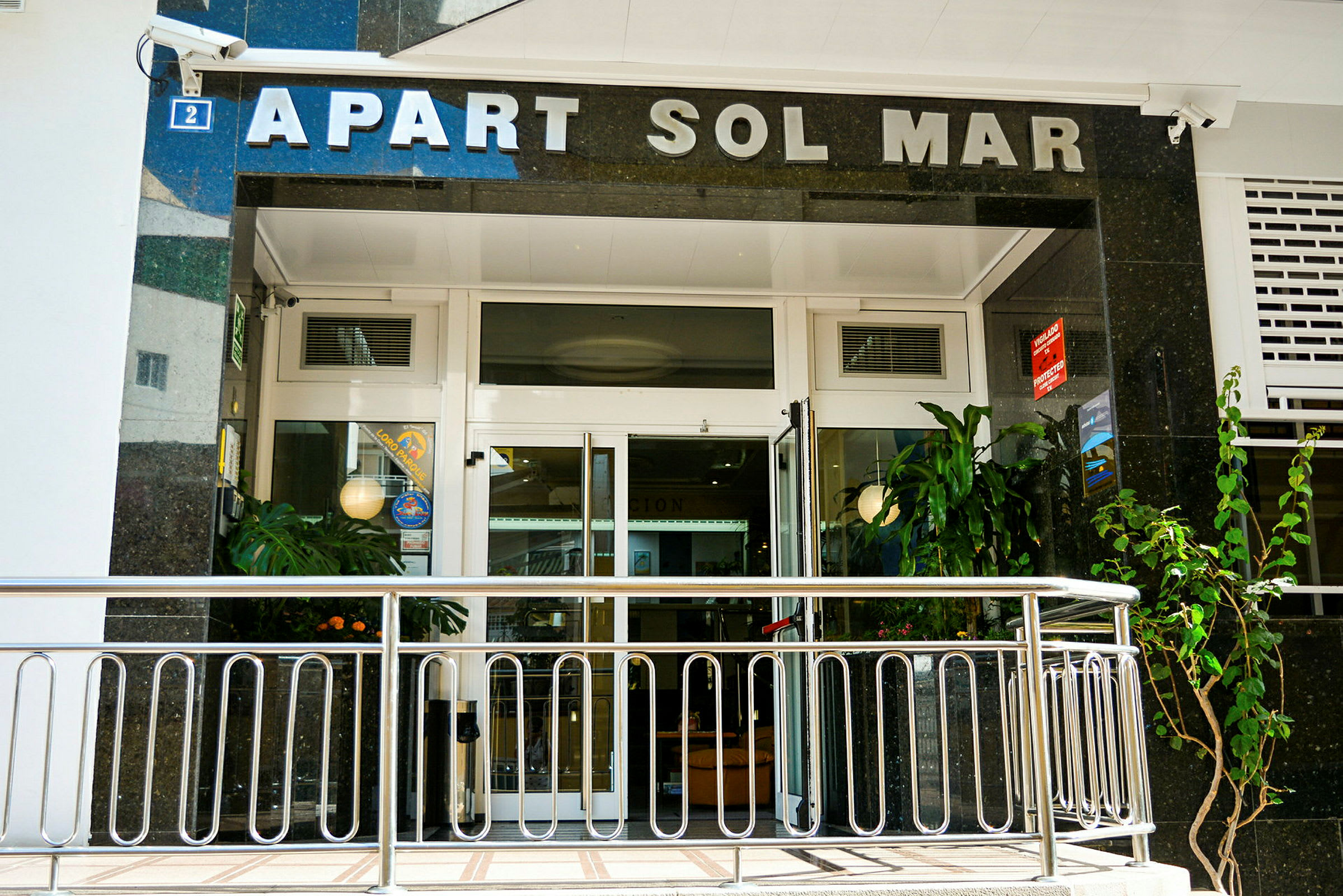 Inngang til Apart Sol Mar med glassdører og planter. (AI-generert tekst)