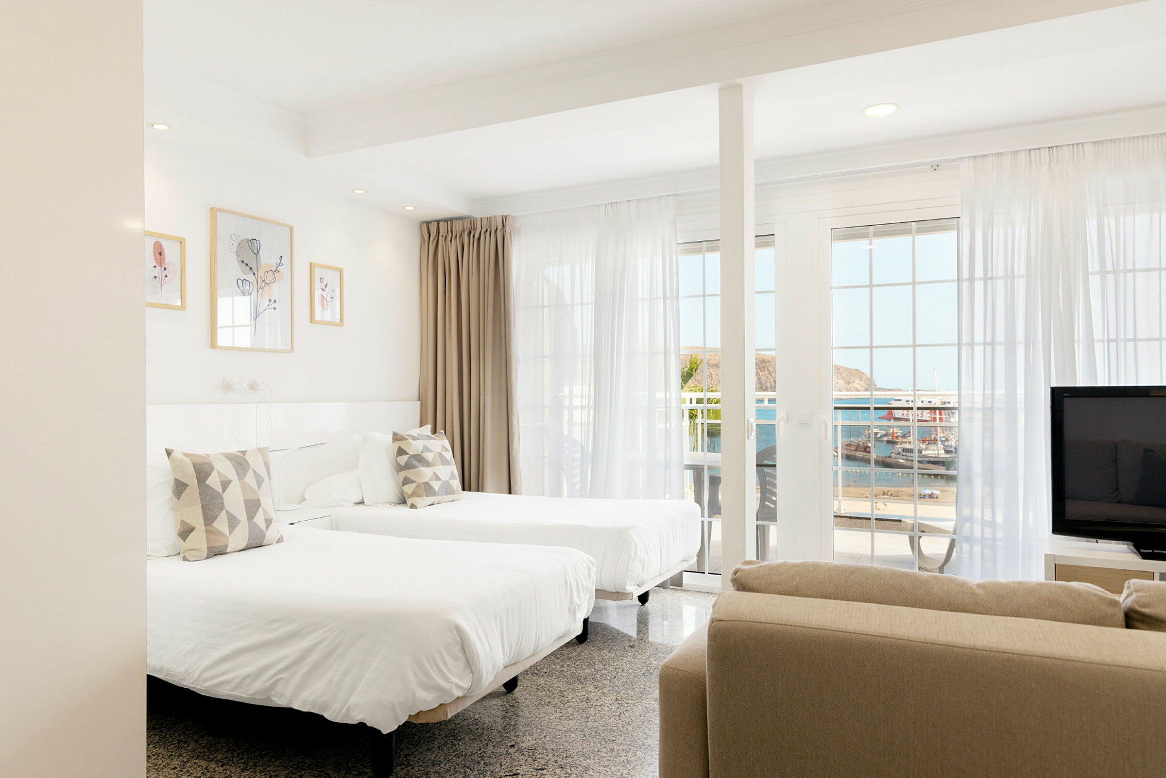 Et lyst hotellrom med to enkeltsenger, store vinduer og havutsikt. (AI-generert tekst)