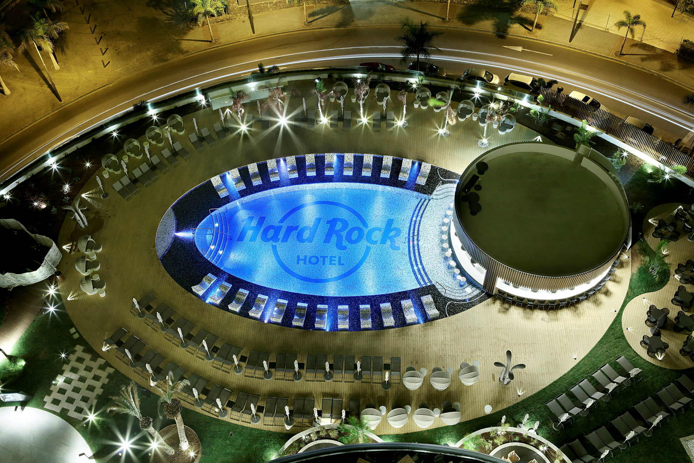 Luftfoto av et opplyst basseng og det omkringliggende området på Hard Rock Hotel om kvelden. (AI-generert tekst)