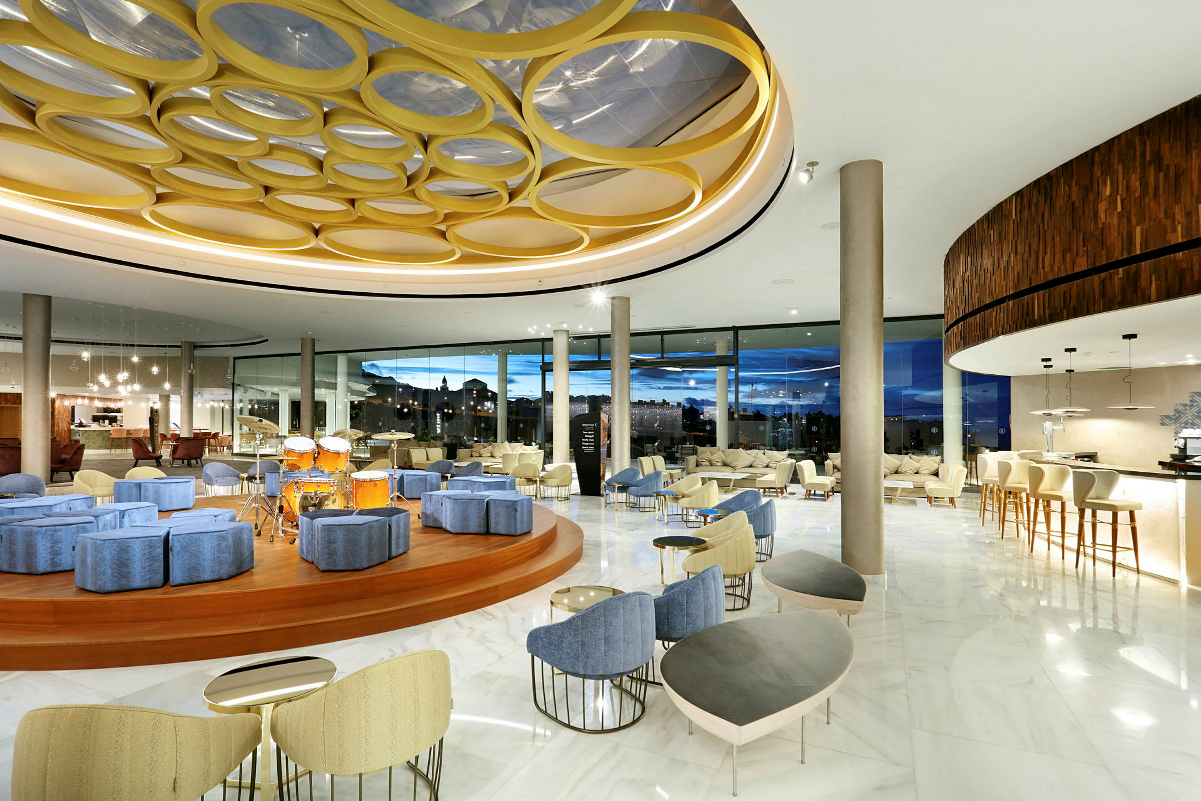 Interiør av en moderne hotellobby med sittegrupper, en scene med trommer og store panoramavinduer. (AI-generert tekst)