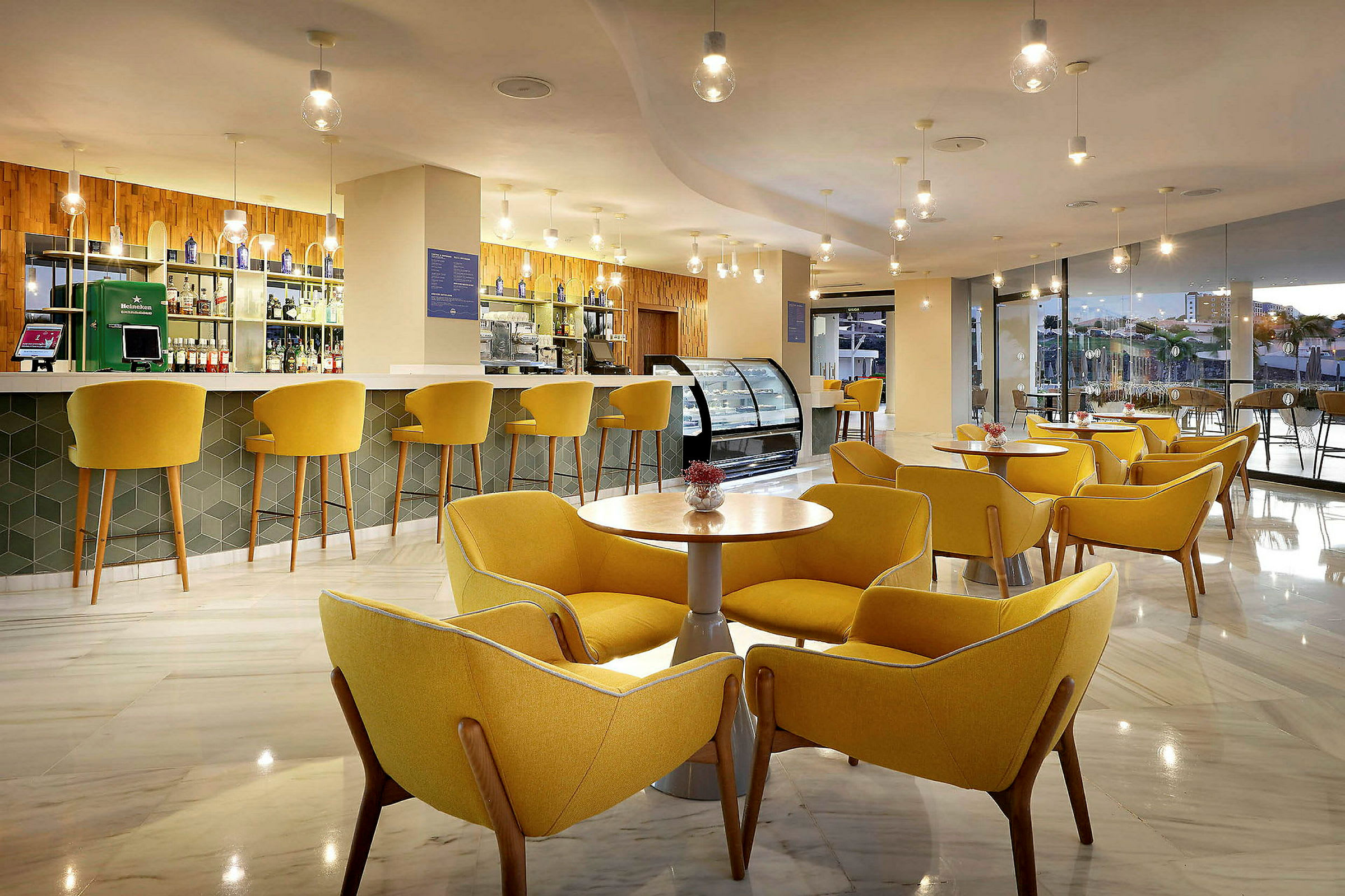 En moderne lounge med gule stoler og bord samt en bar i bakgrunnen. (AI-generert tekst)