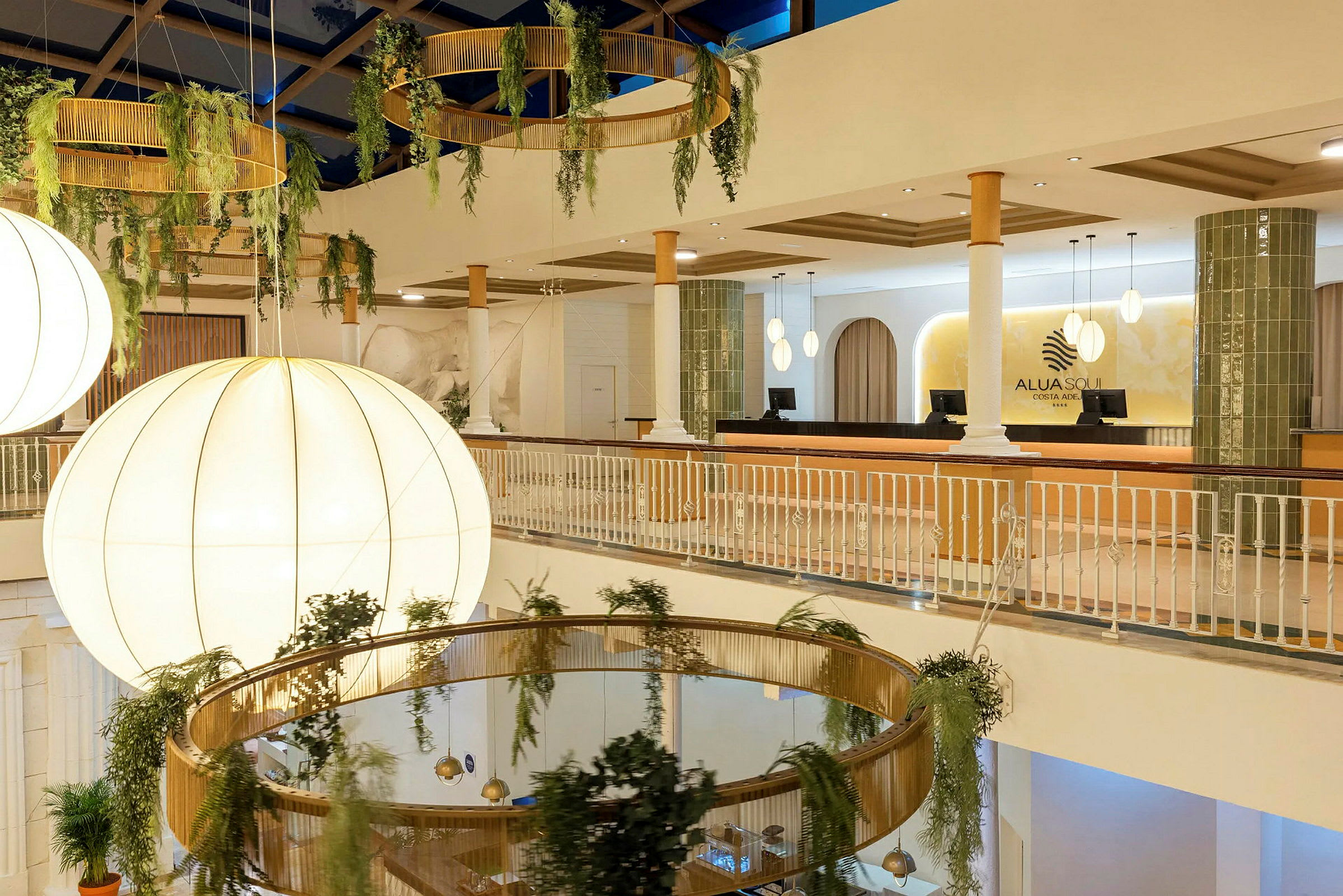 Interiør av en hotellobby med store lysekroner, hengende plantepynt og resepsjonen synlig. (AI-generert tekst)