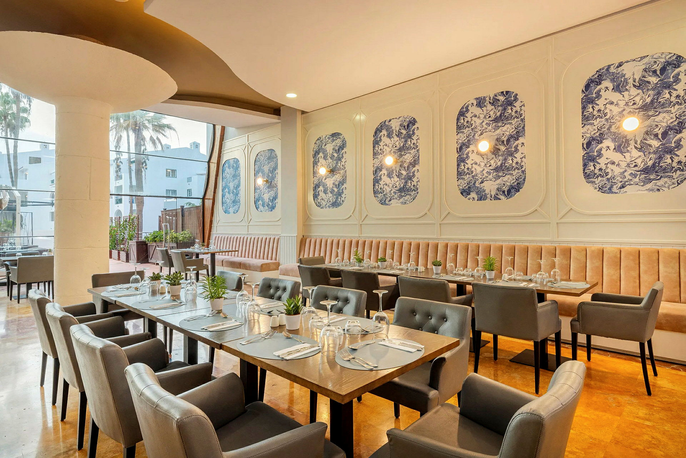Interiør av en restaurant med elegante bord og stoler, samt blå dekorasjoner på veggen. (AI-generert tekst)