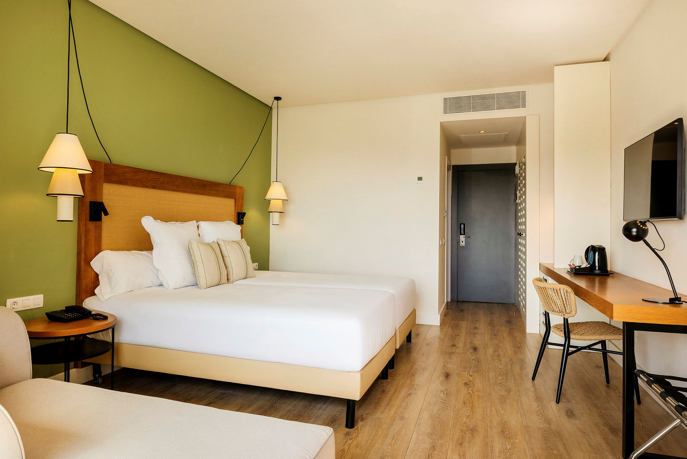 Hotellrom med en bred seng, skrivebord og grønn vegg. (AI-generert tekst)