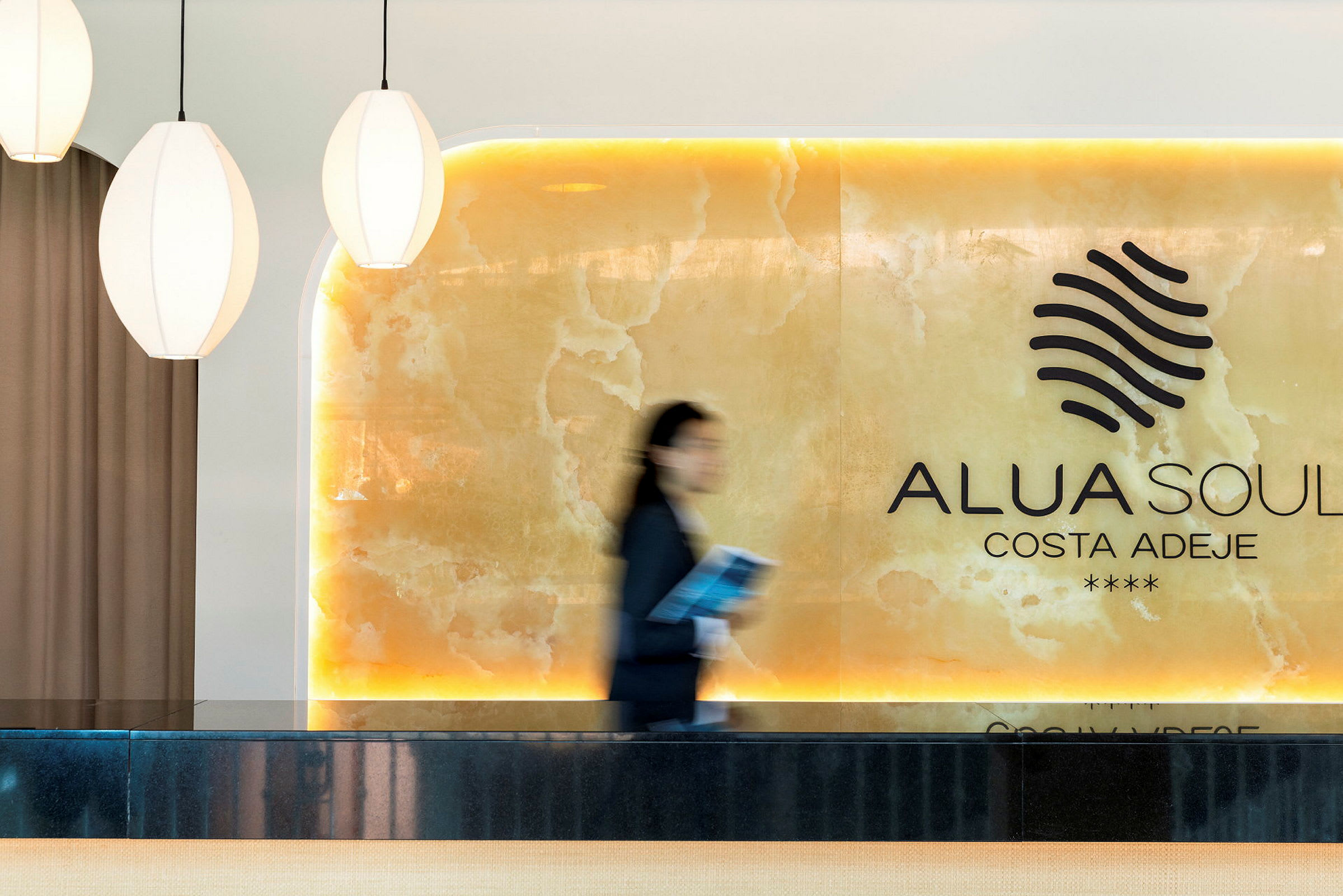 Resepsjonen på Alua Soul Costa Adeje vises med lyse detaljer og en person i bevegelse. (AI-generert tekst)