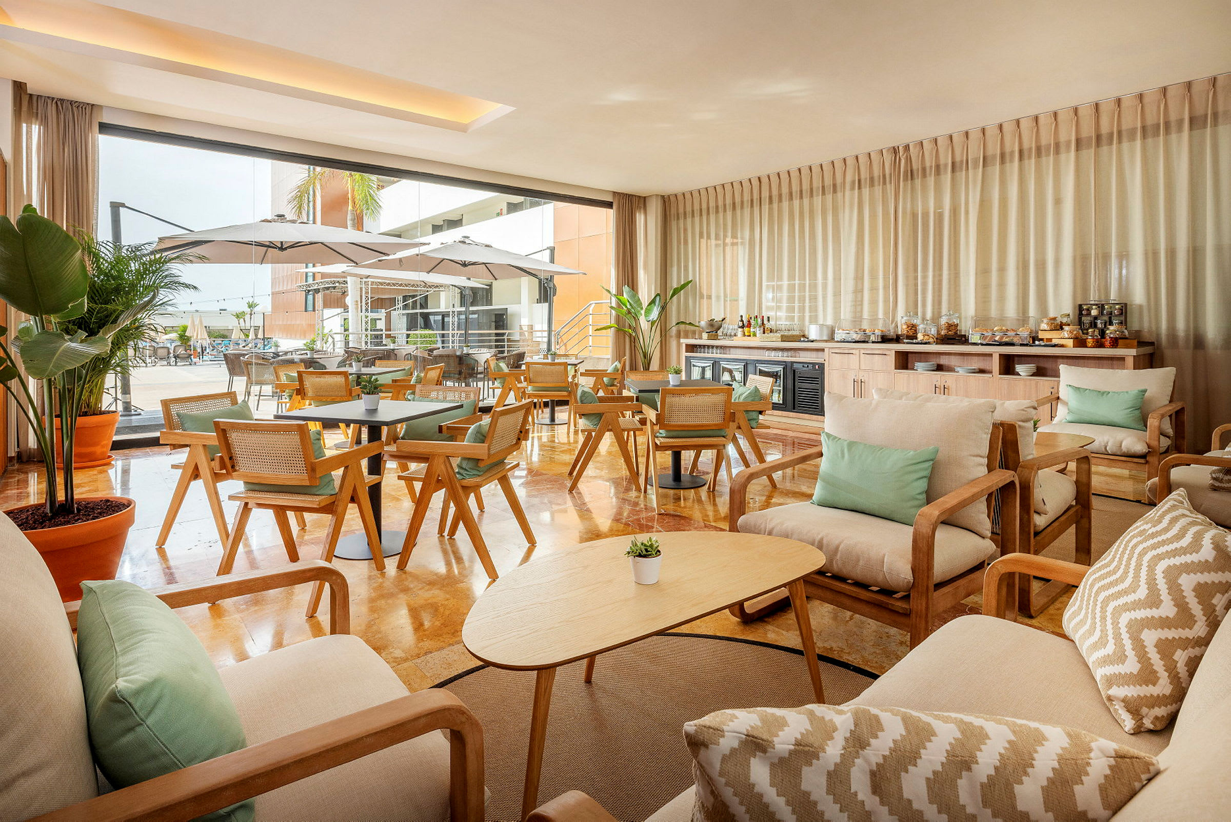 En elegant lounge med tremøbler og stoffputer. Utsikt mot et utendørs basseng med parasoller. (AI-generert tekst)