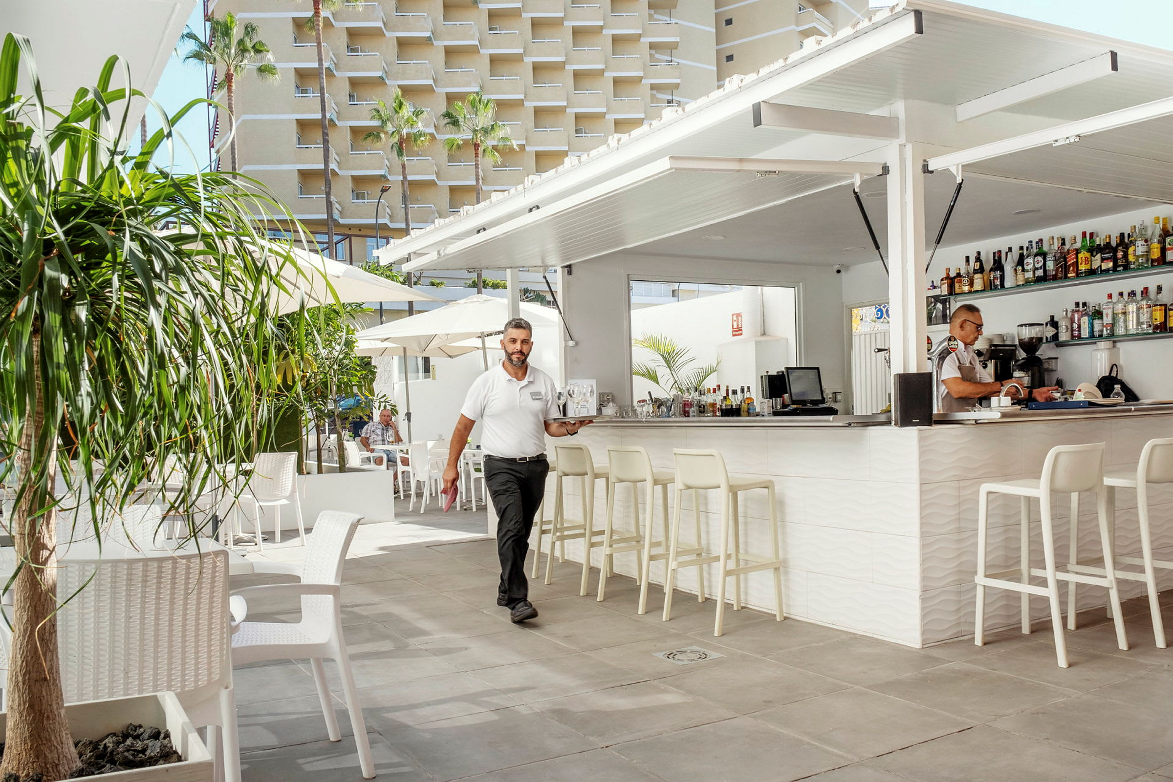 Bilde av en utendørs bar med sitteplasser, parasoller og en bygning i bakgrunnen. (AI-generert tekst)