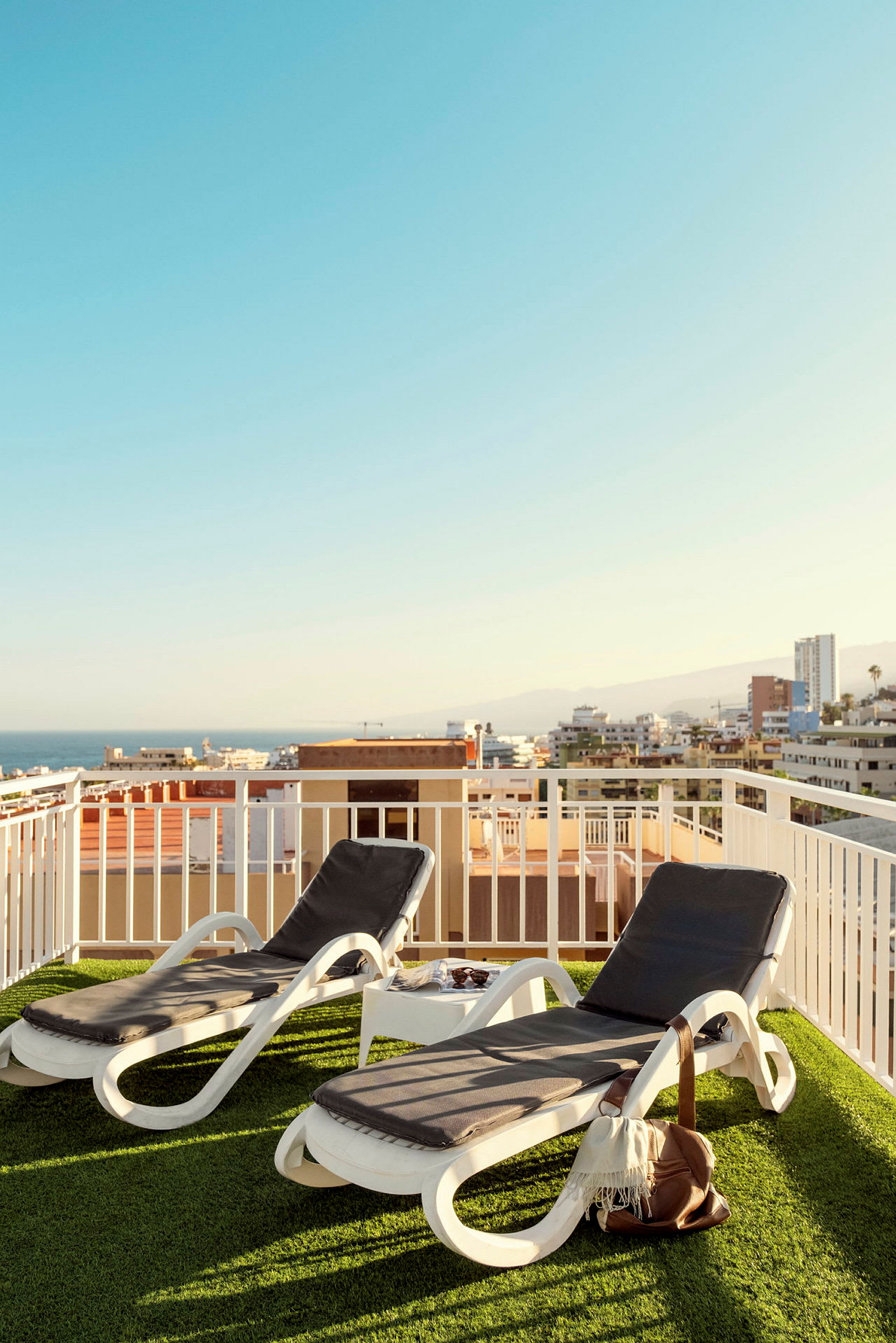 To solsenger på en terrasse med utsikt over bygninger og hav. (AI-generert tekst)