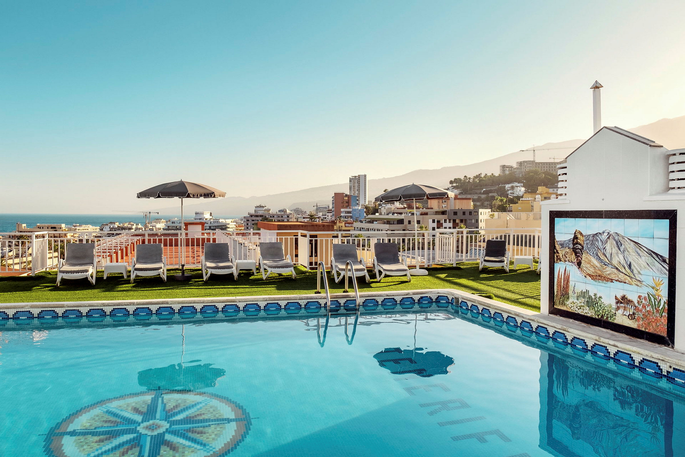 Bilde av et basseng med solsenger på takterrassen og utsikt over en by. (AI-generert tekst)