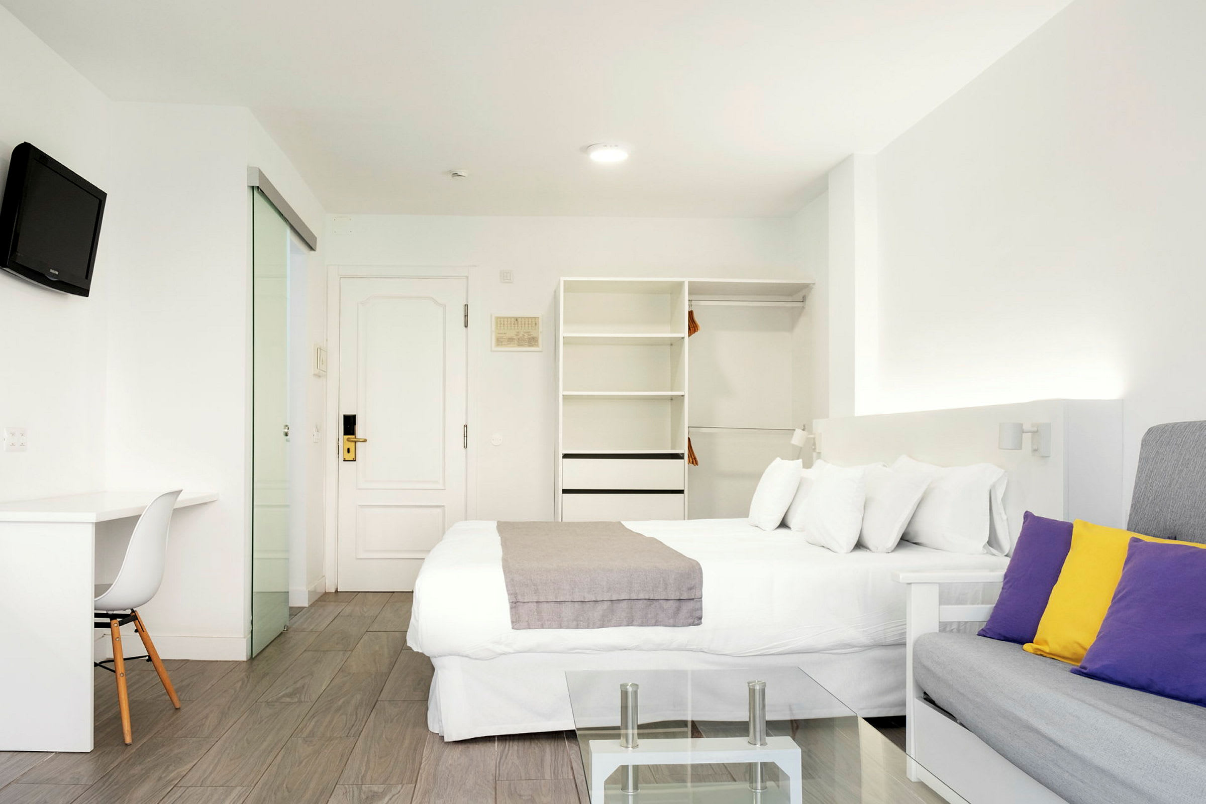 Moderne hotellrom med hvitt interiør og fargerike puter. (AI-generert tekst)