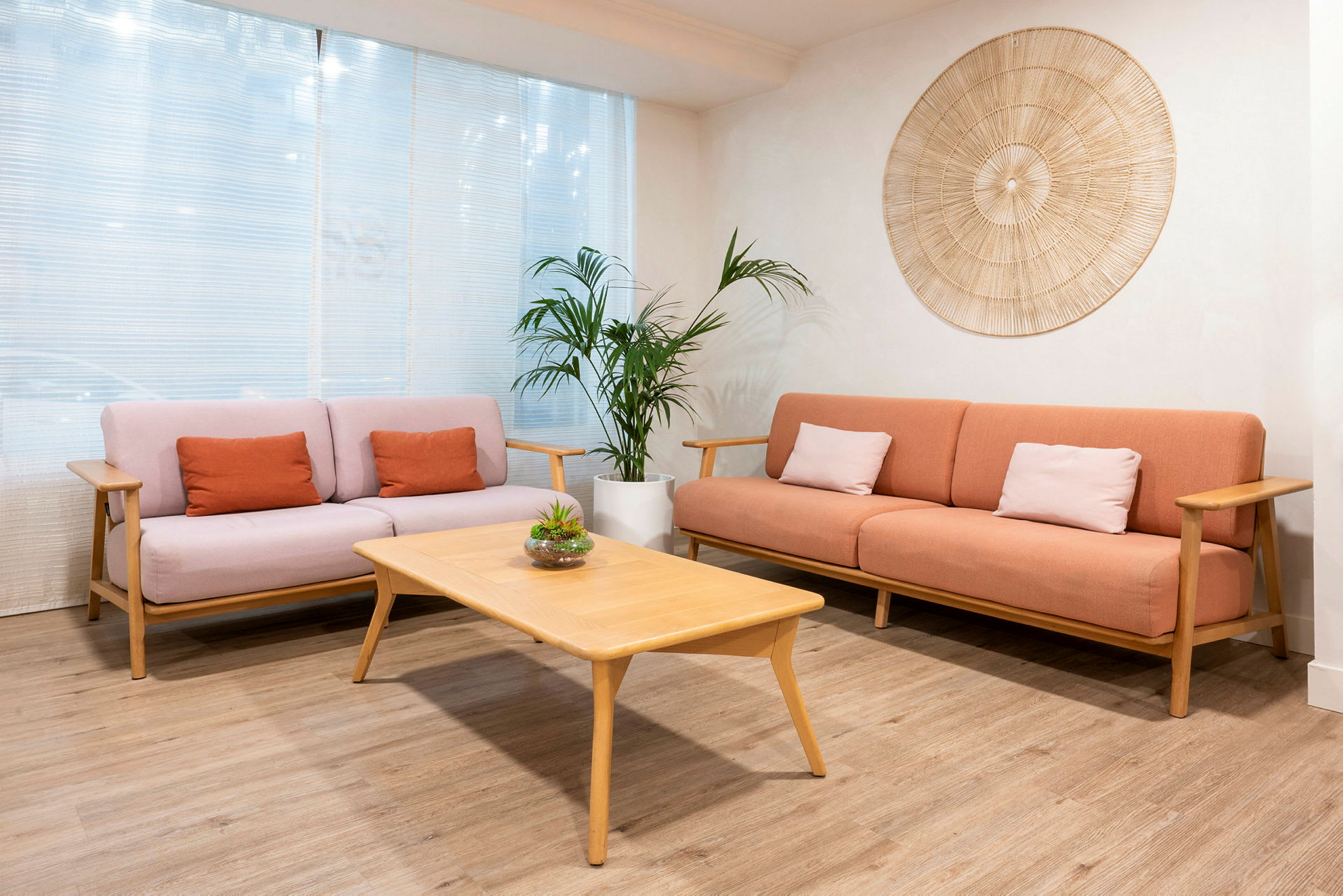 To sofaer med fargerike puter og et trebord i et rom med planter og dekor på veggen. (AI-generert tekst)