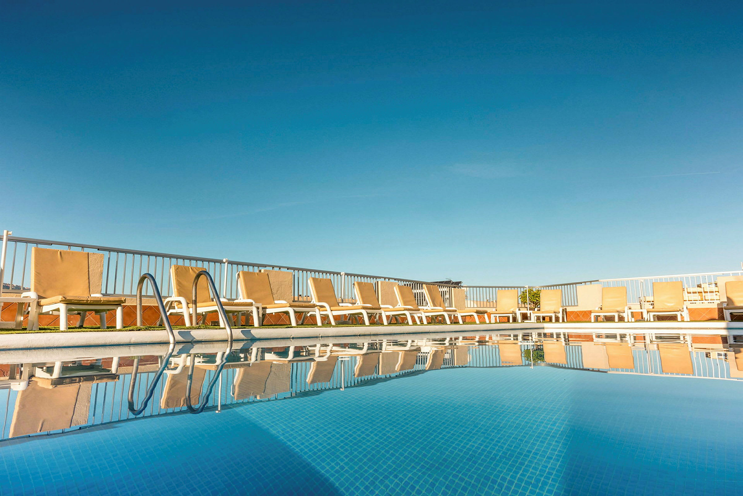 Solstoler og basseng på et hotell med klar blå himmel. (AI-generert tekst)
