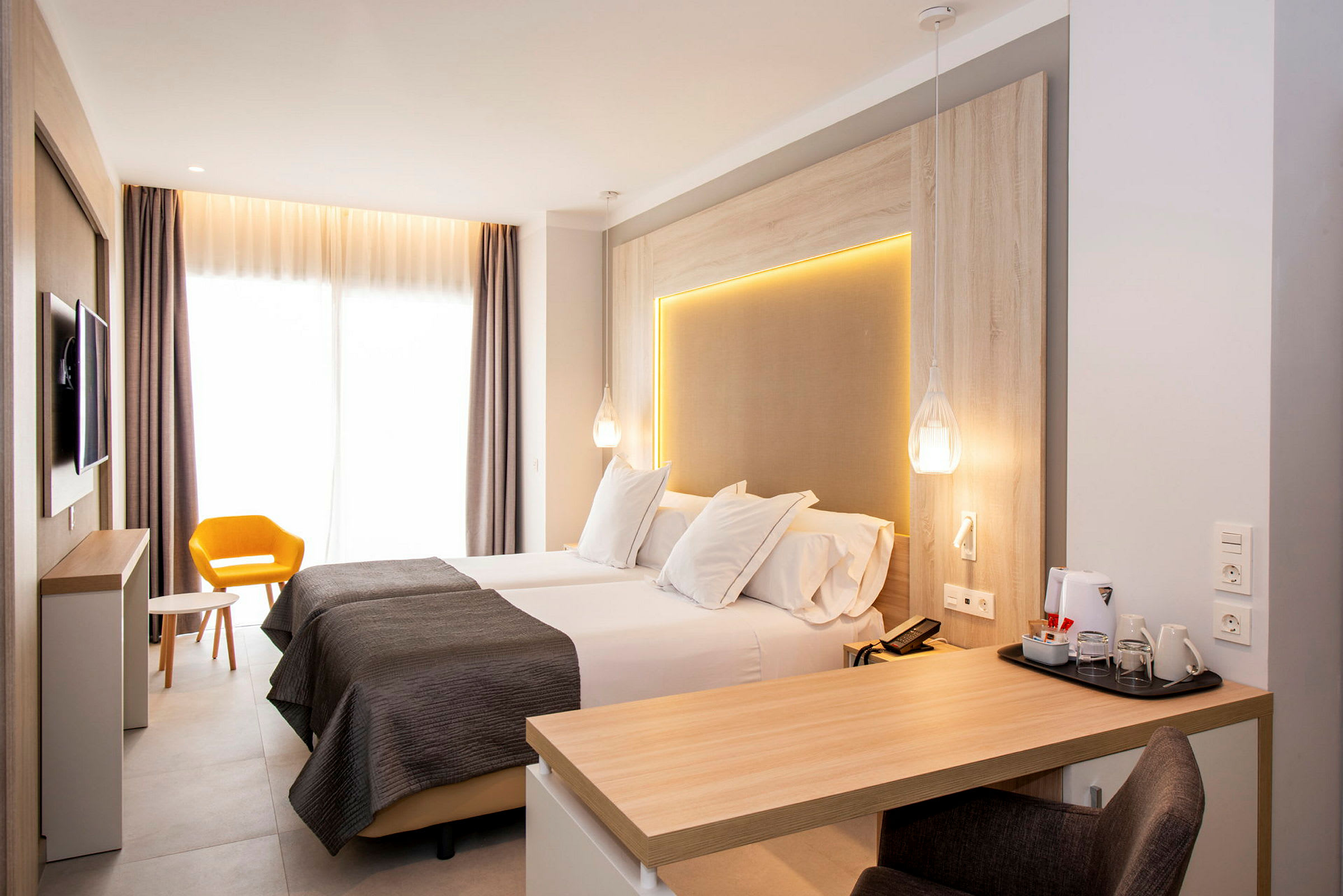 Moderne hotellrom med to enkeltsenger, skrivebord og gul stol. (AI-generert tekst)