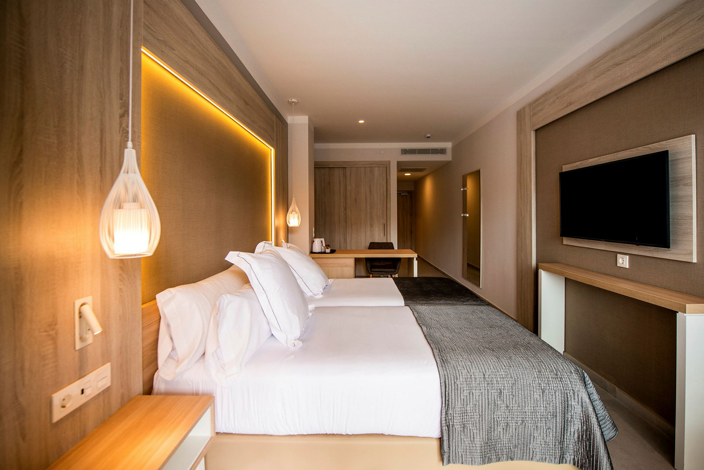 Hotellrom med dobbeltseng, veggmontert TV og skrivebord. (AI-generert tekst)