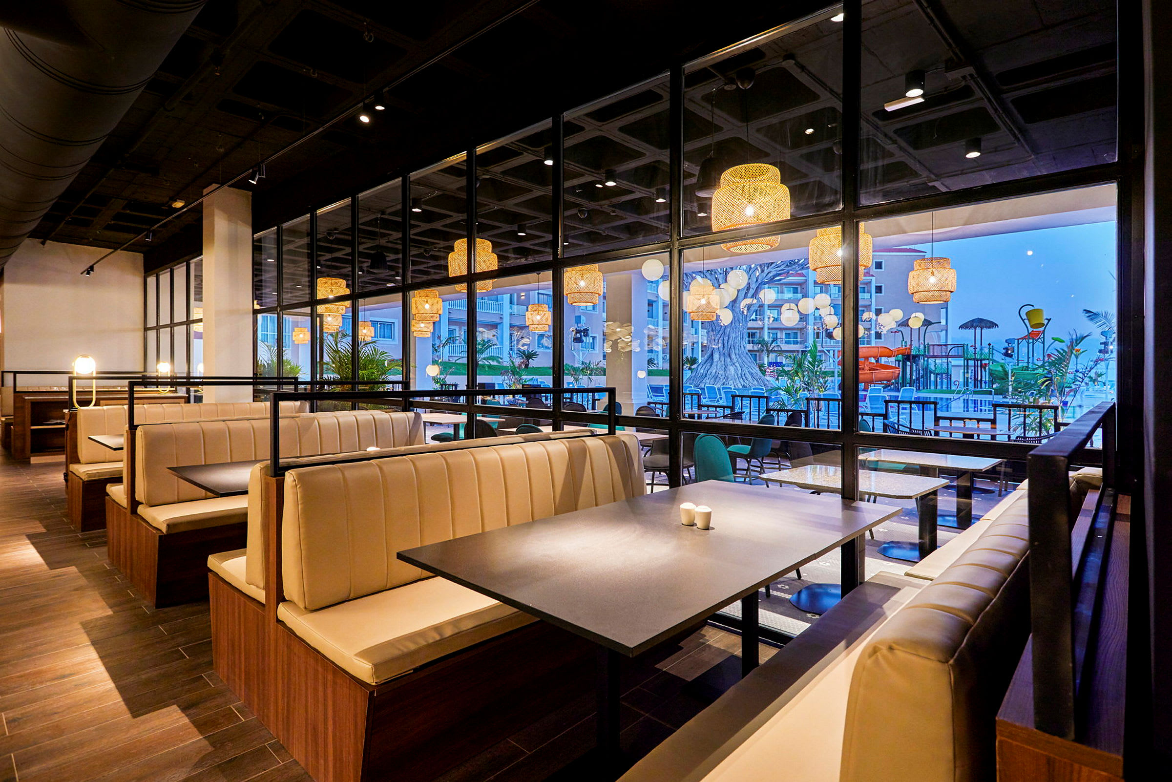 En moderne restaurant med lyse båser og store vinduer som vender ut mot en terrasse med basseng og dekorasjoner. (AI-generert tekst)