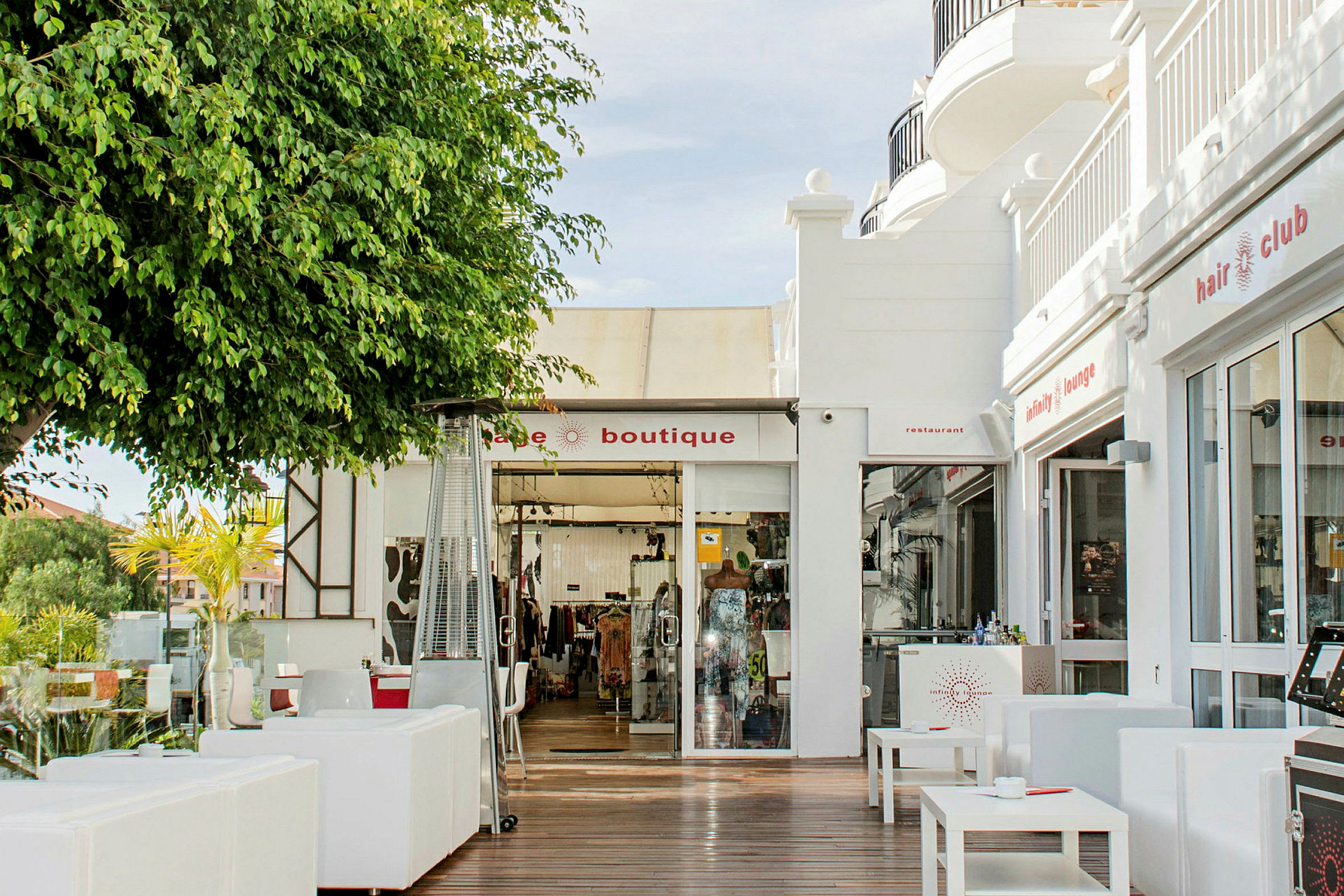 Bilde av en butikk og restaurant med utemøbler i et solrikt miljø. (AI-generert tekst)