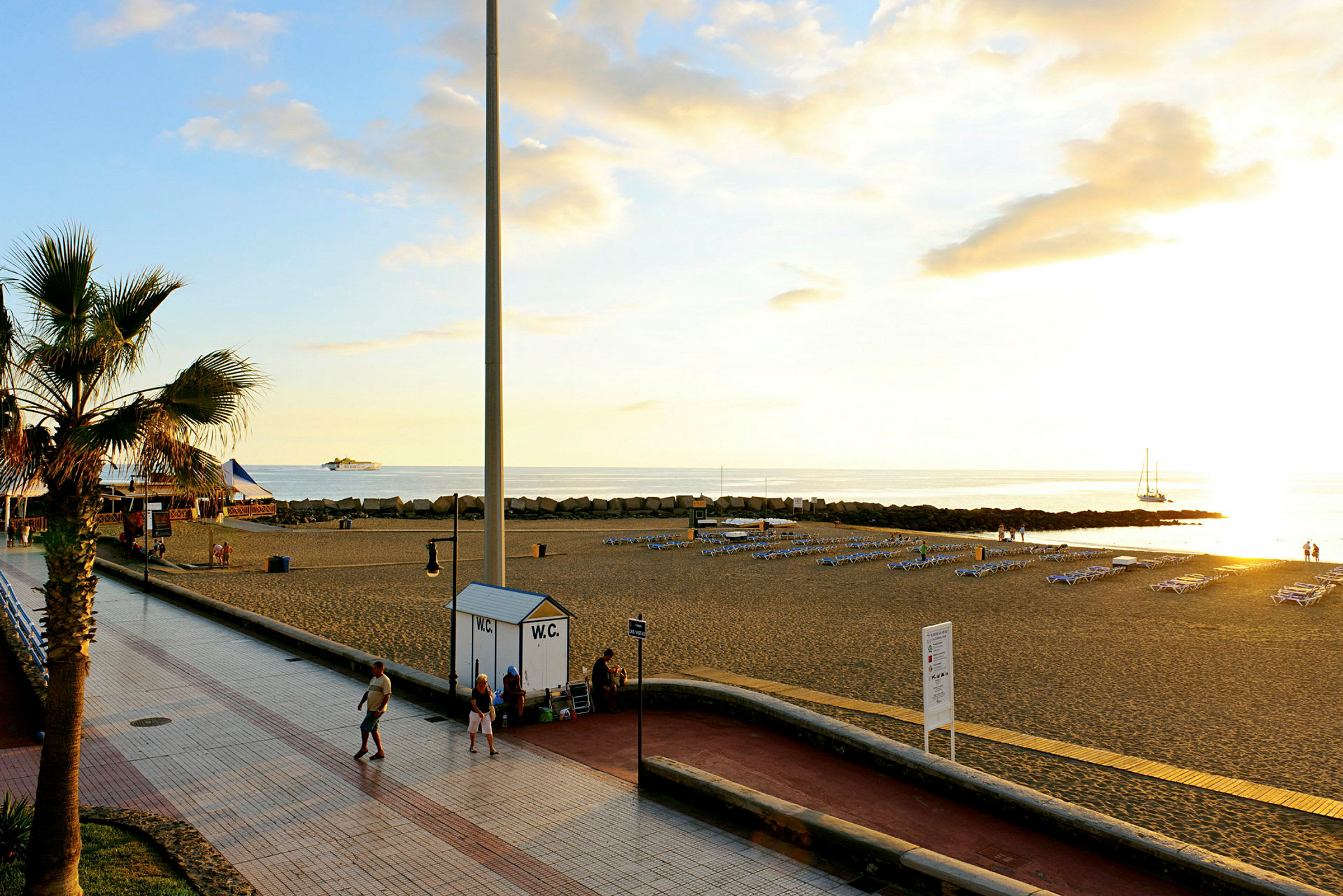 Strandpromenade med palmer og hav i solnedgang. (AI-generert tekst)