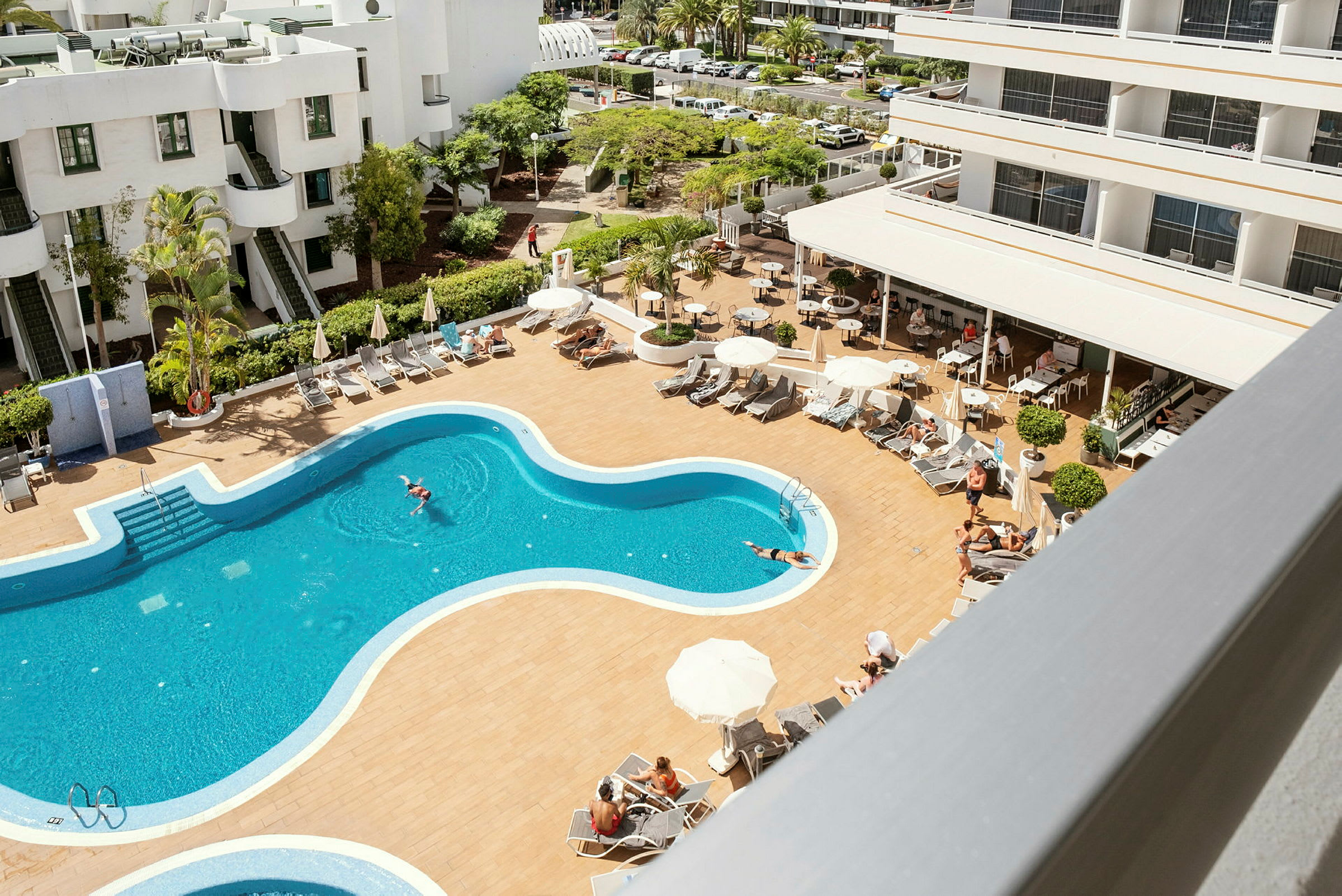 Bilde av et hotellbasseng med solsenger og parasoller, omgitt av hotellbygninger. (AI-generert tekst)