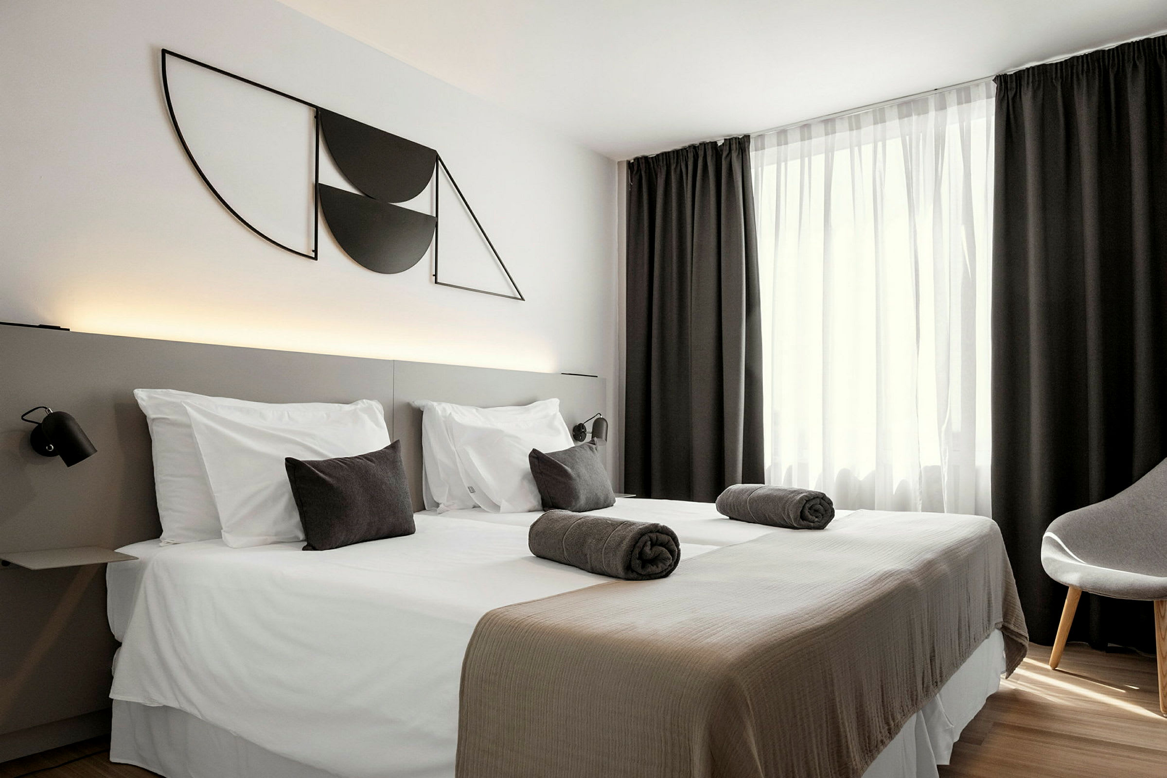 Et hotellrom med to enkeltsenger, mørke gardiner og moderne veggdekor. (AI-generert tekst)