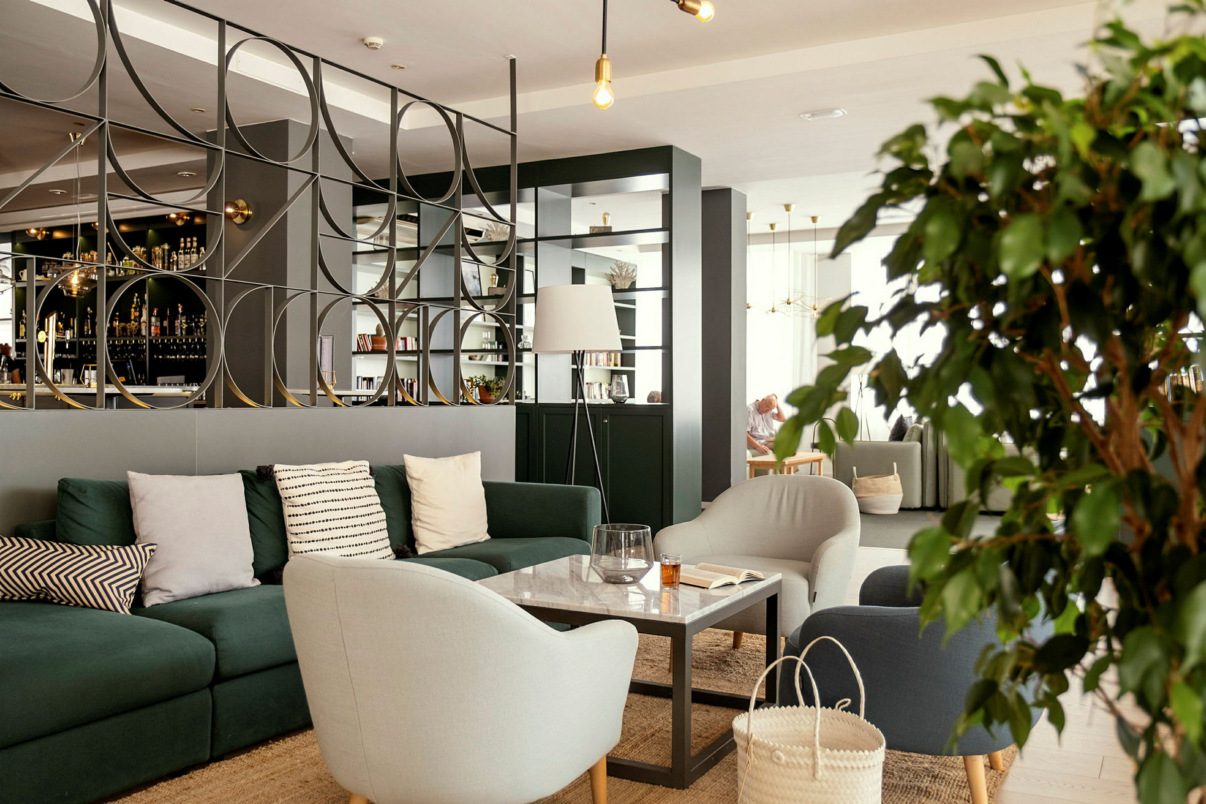 En moderne lounge med sofaer, lenestoler og et bord foran en dekorativ skille. (AI-generert tekst)