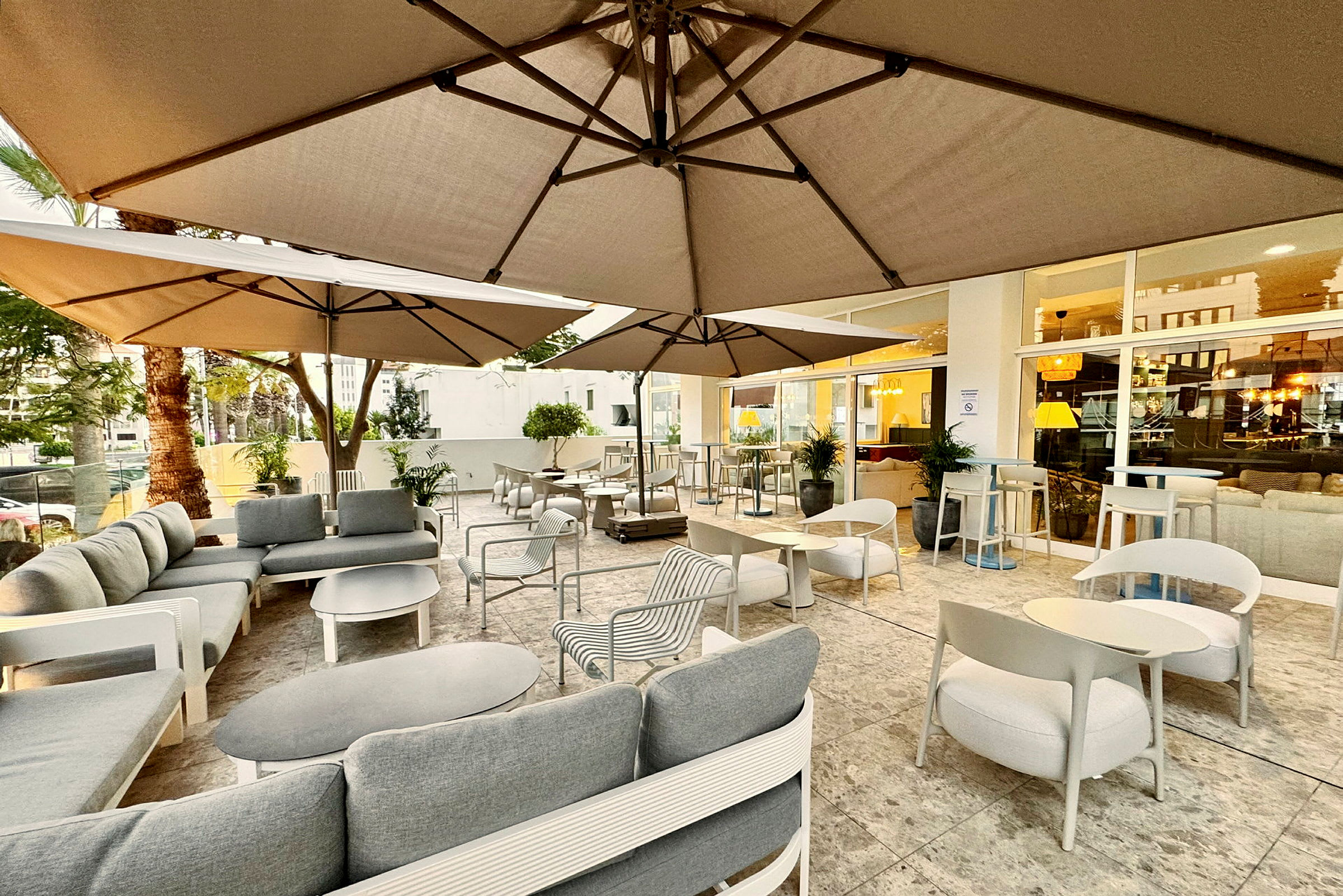Utendørs serveringsområde med sofaer og bord under parasoller. (AI-generert tekst)