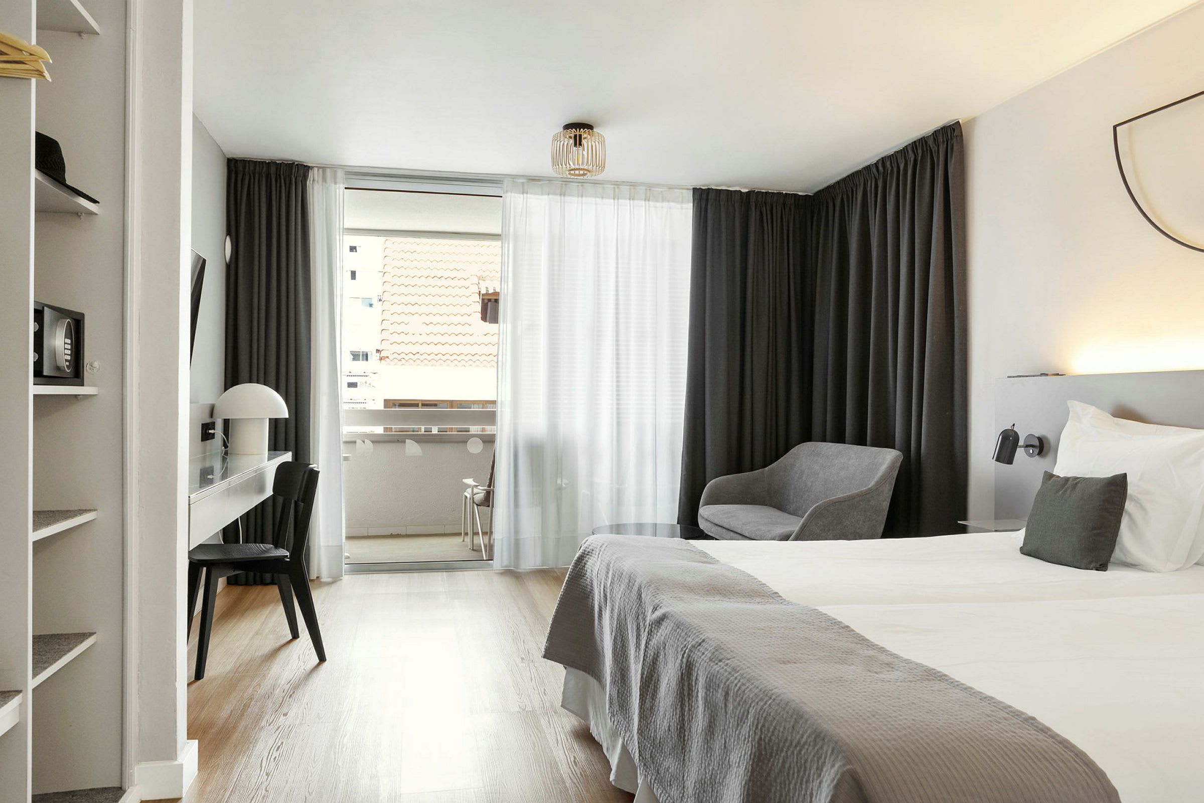 Et hotellrom med dobbeltseng, skrivebord, stol og sittegruppe; utsikt mot en balkong med takutsikt. (AI-generert tekst)