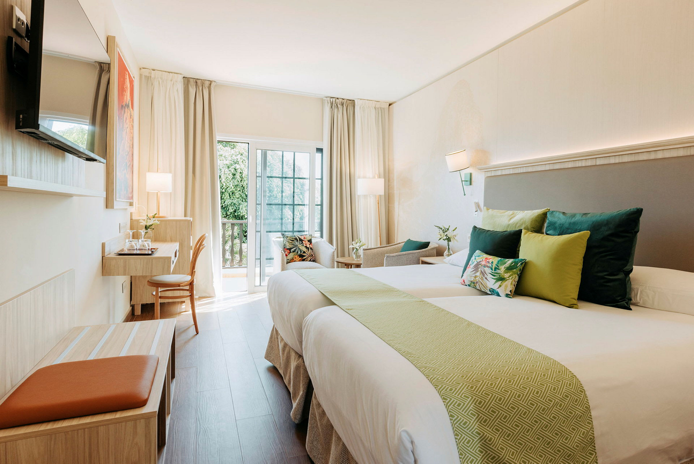Et lyst hotellrom med to senger, pynteputer og en arbeidsstasjon ved balkongen. (AI-generert tekst)
