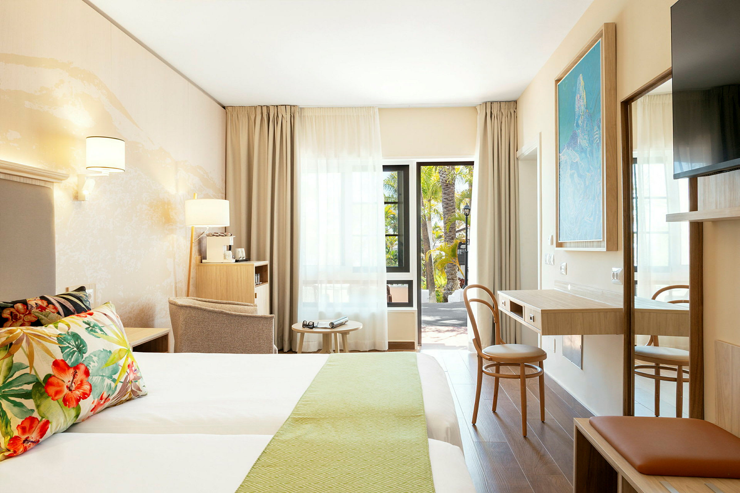 Bilde av et moderne hotellrom med dobbeltseng, skrivebord og sittemøbler, samt en åpen dør mot en balkong. (AI-generert tekst)