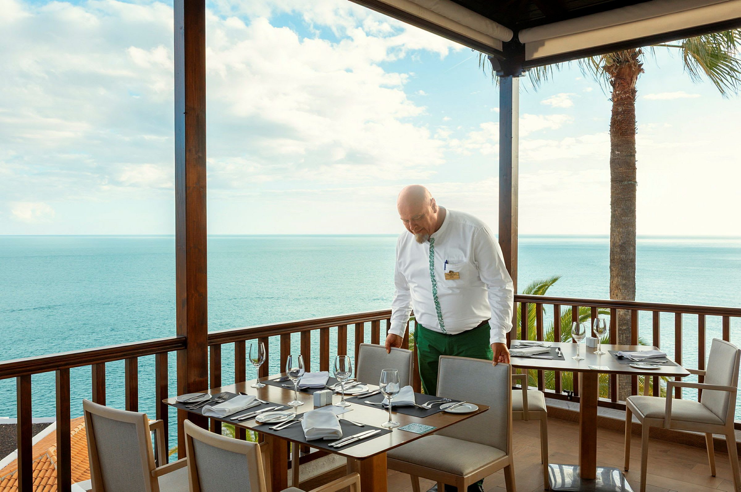 En spisesal med dekkede bord på en terrasse med utsikt over havet. (AI-generert tekst)