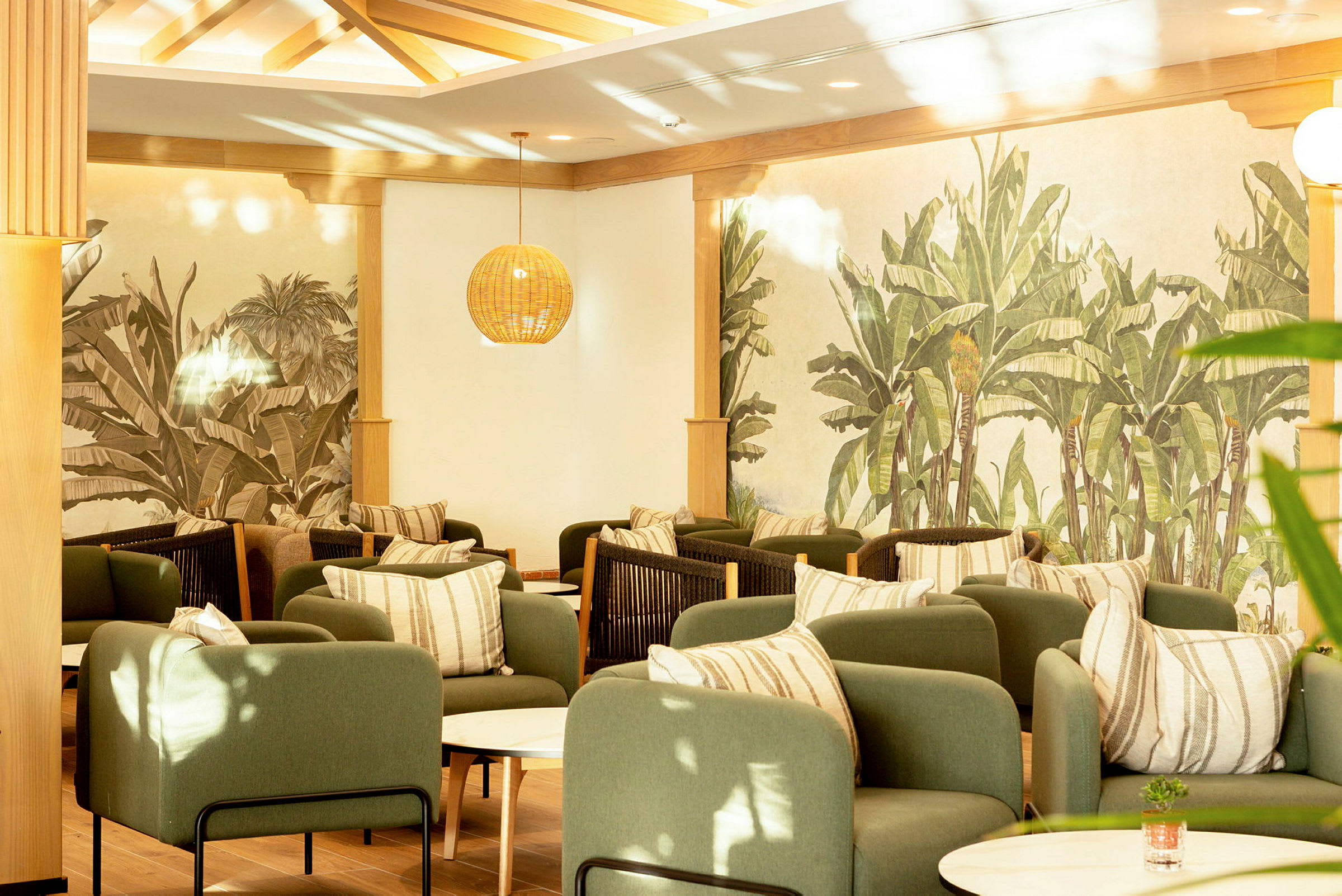 En elegant lounge med grønne lenestoler, stripete puter og vegger dekorert med planteillustrasjoner. (AI-generert tekst)
