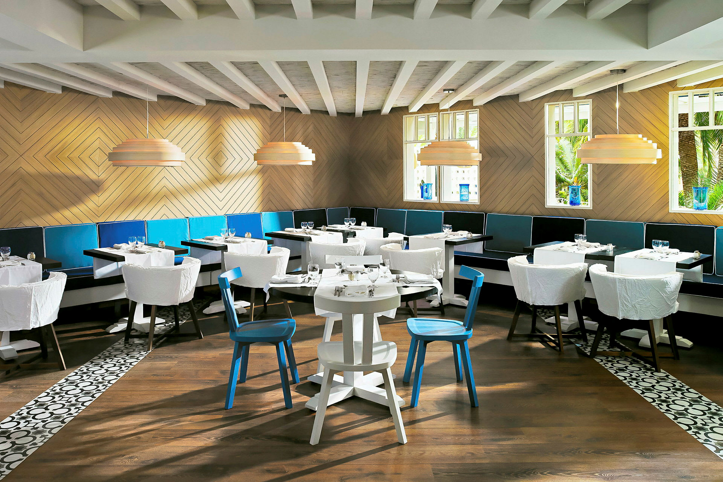 Et lyst, moderne restaurantrom med flere bord og stoler, trevegger og store vinduer. (AI-generert tekst)