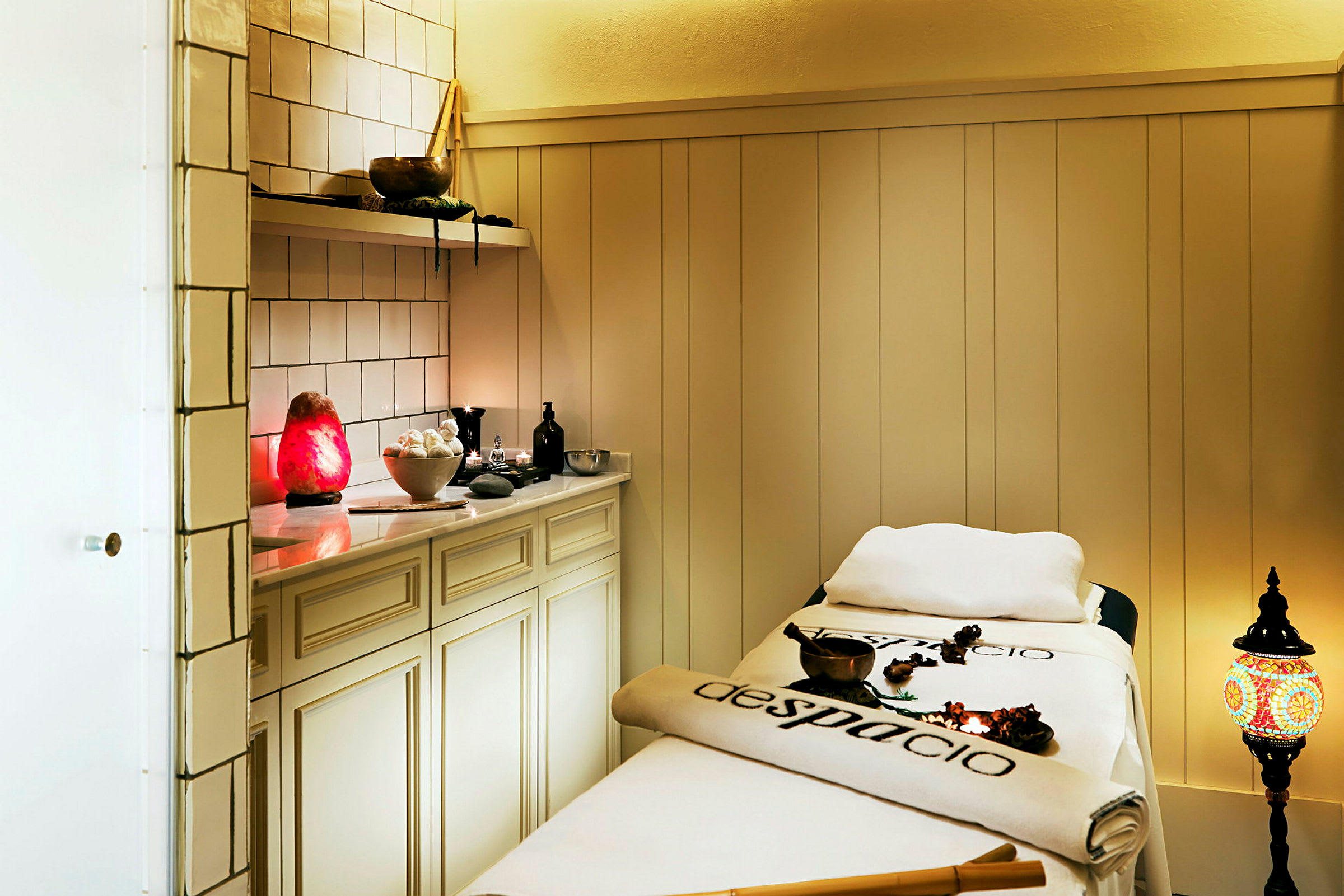 Bilde av et spa-rom med behandlingsseng, skap og dekorative gjenstander, inkludert en rød lampe og en fargerik lykt. (AI-generert tekst)