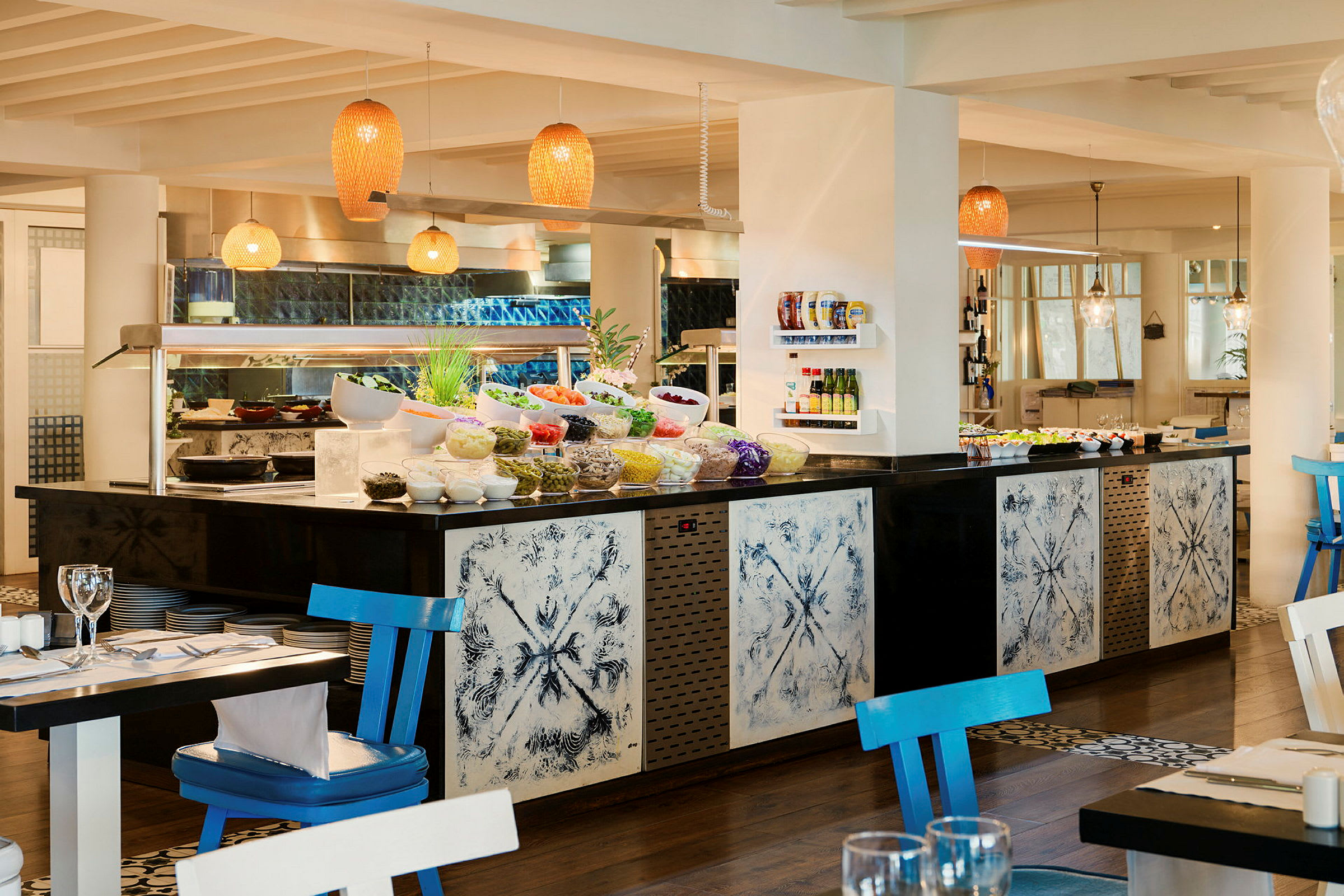 Et bilde av en buffet i en restaurant med lys og åpen innredning. Fargerik mat og skåler med ulike retter er plassert foran dekorative paneler. (AI-generert tekst)