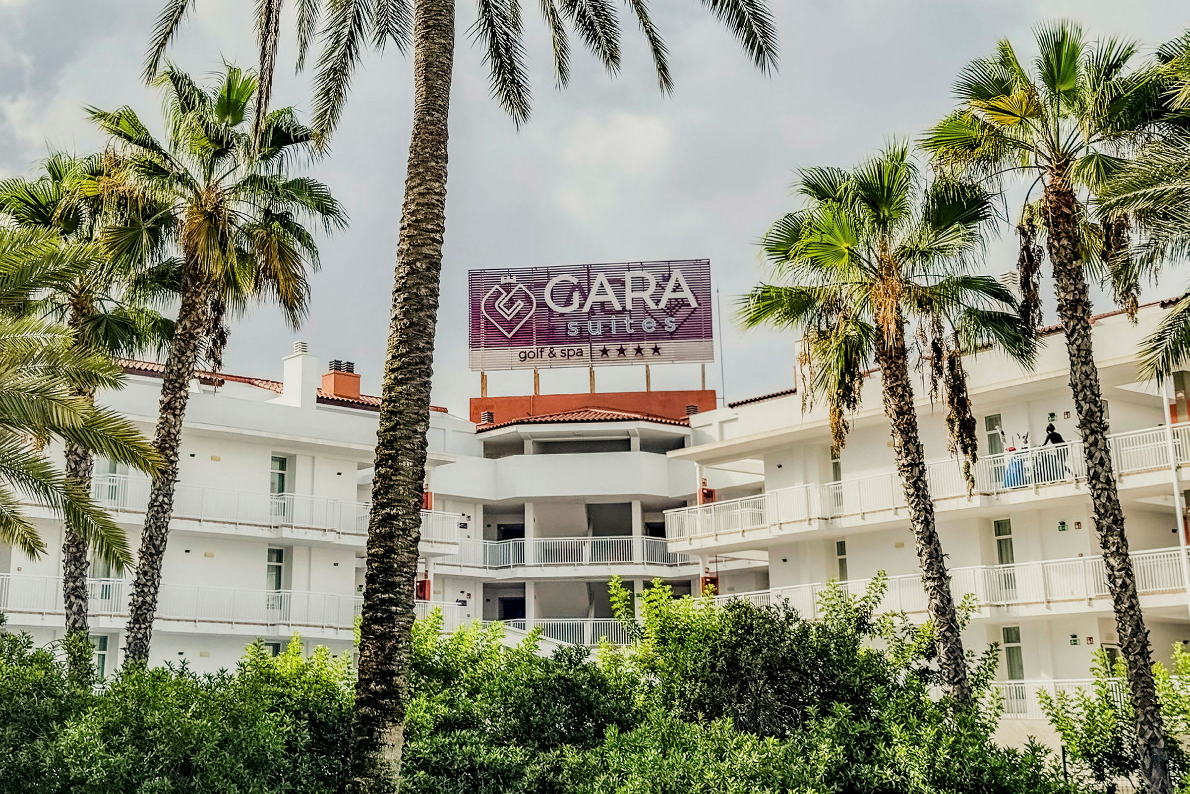 En bygning med balkonger og et skilt som sier "Gara Suites Golf & Spa" omgitt av palmer. (AI-generert tekst)