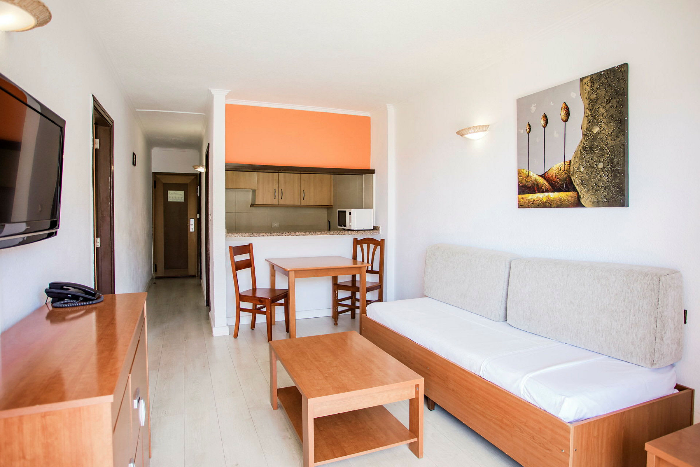 Leilighetsinteriør med en sofa, et bord, to stoler og et åpent kjøkken med oransje vegg. (AI-generert tekst)
