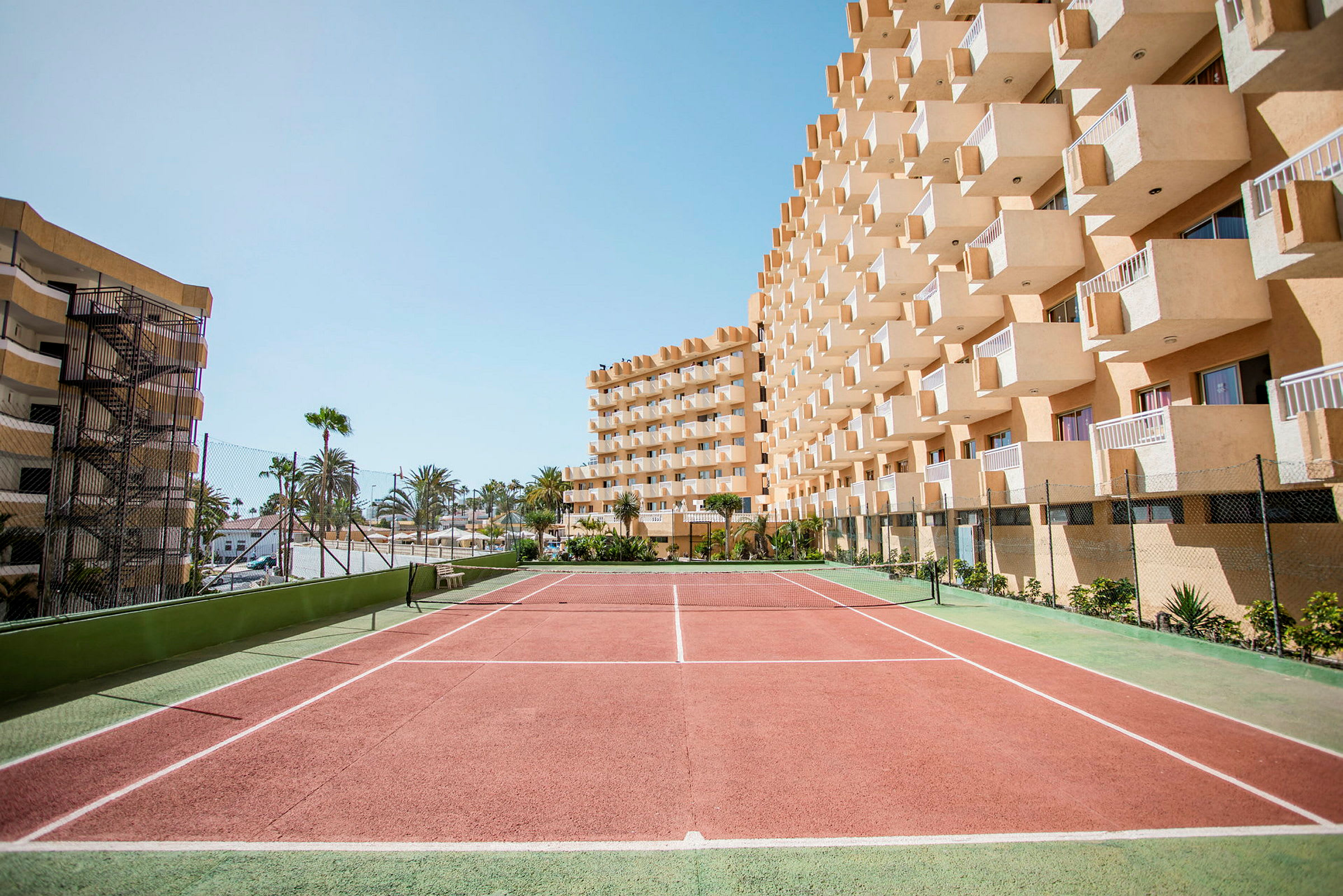 En tennisbane foran en hotellbygning med balkonger. (AI-generert tekst)