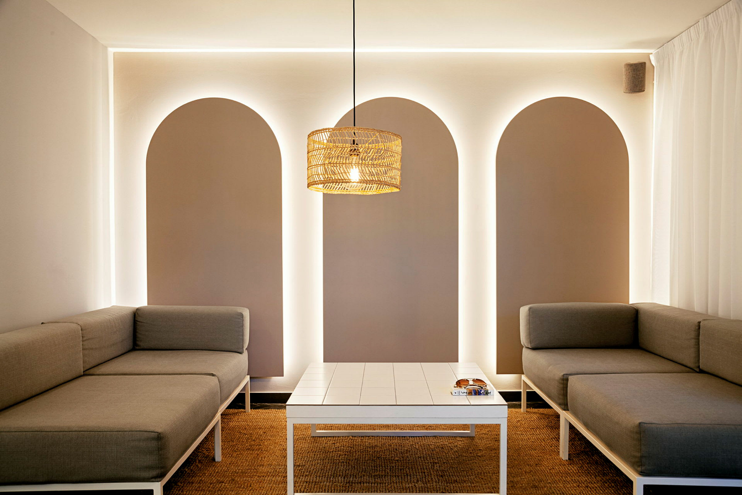 Moderne innredet rom med grå sofaer og et hvitt bord, opplyst av en taklampe. (AI-generert tekst)