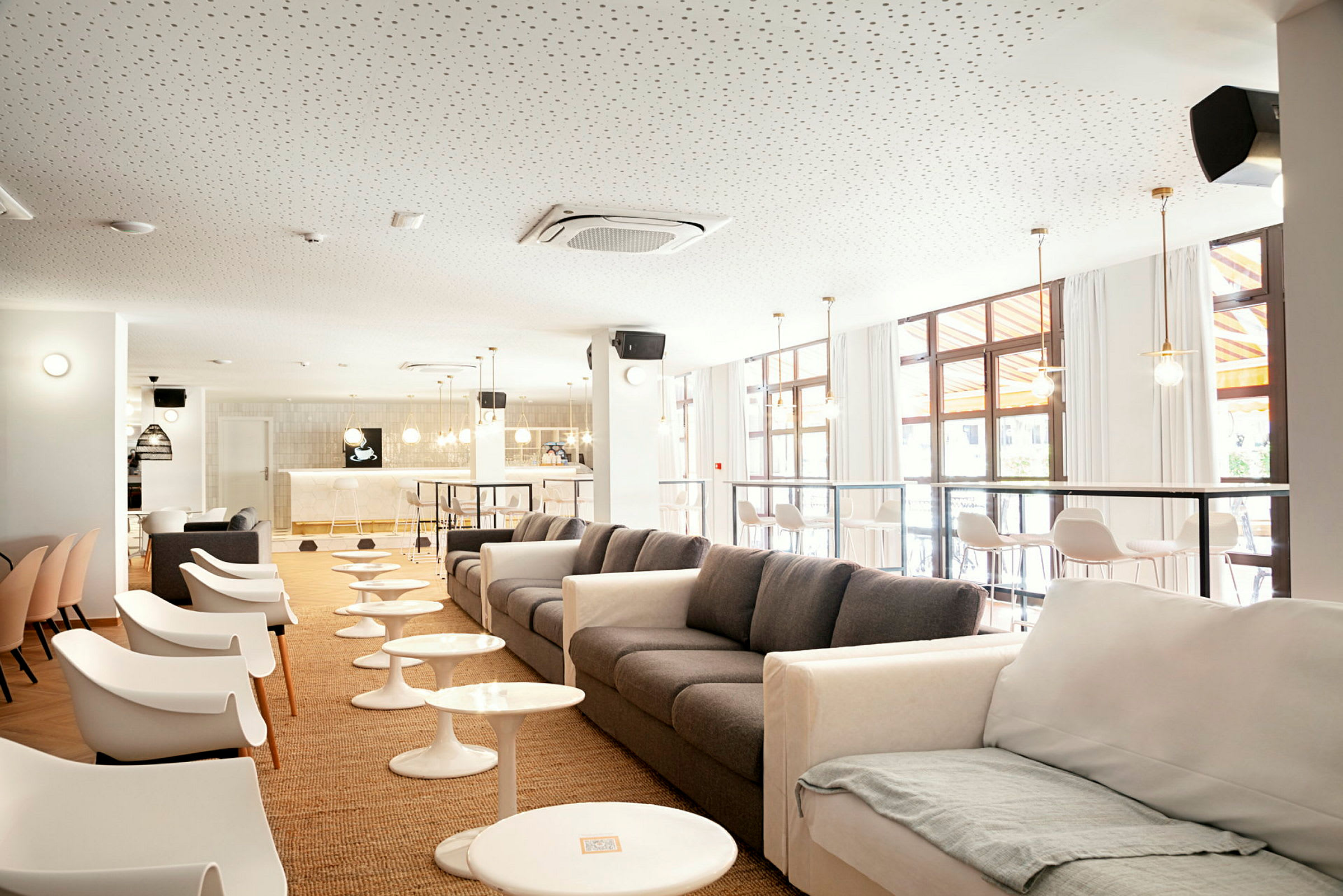 En moderne lounge med sofaer og stoler, små bord og en bar i bakgrunnen. (AI-generert tekst)